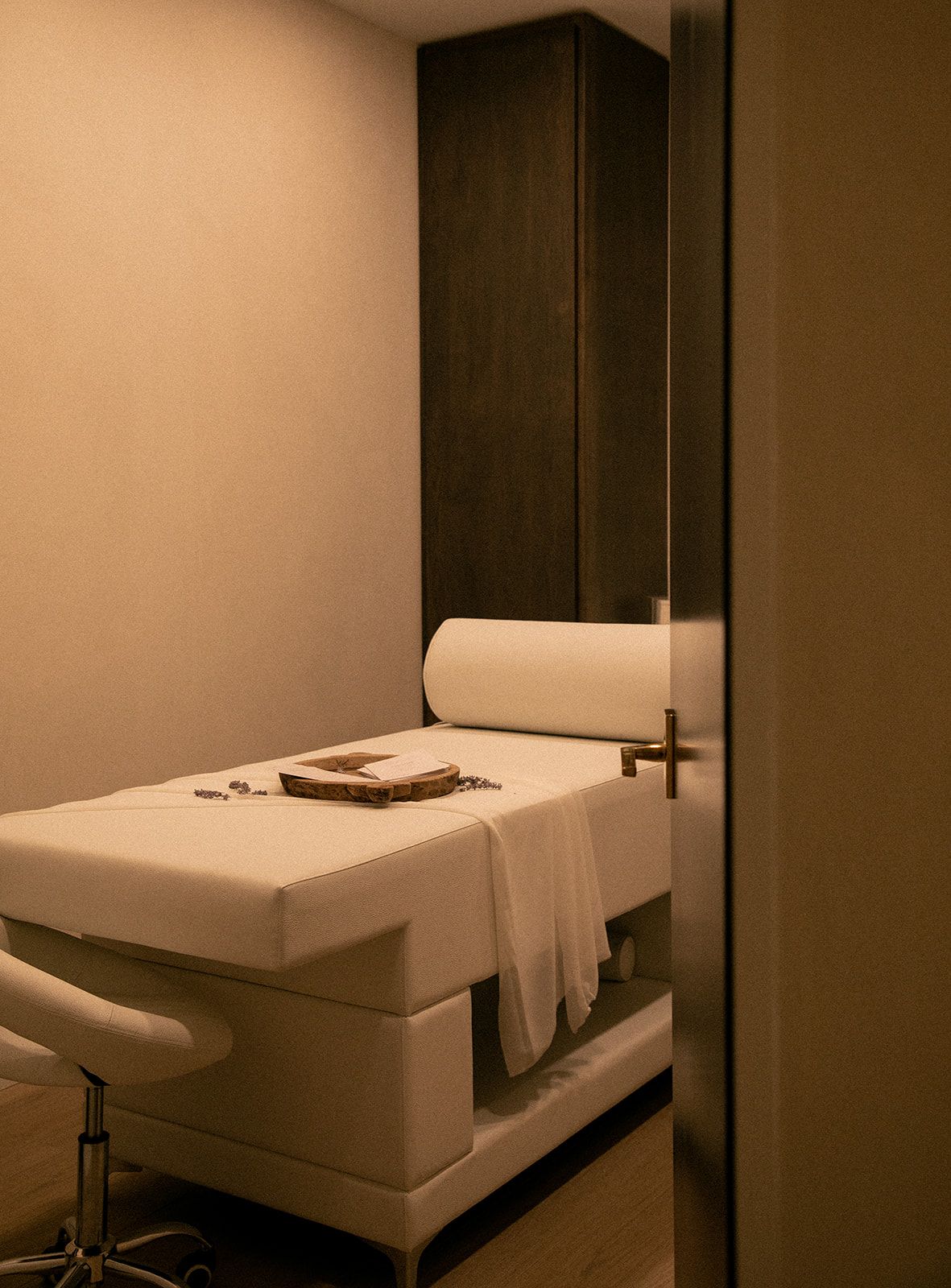 Minimalist spa treatment room with white massage table and dark wood paneling.