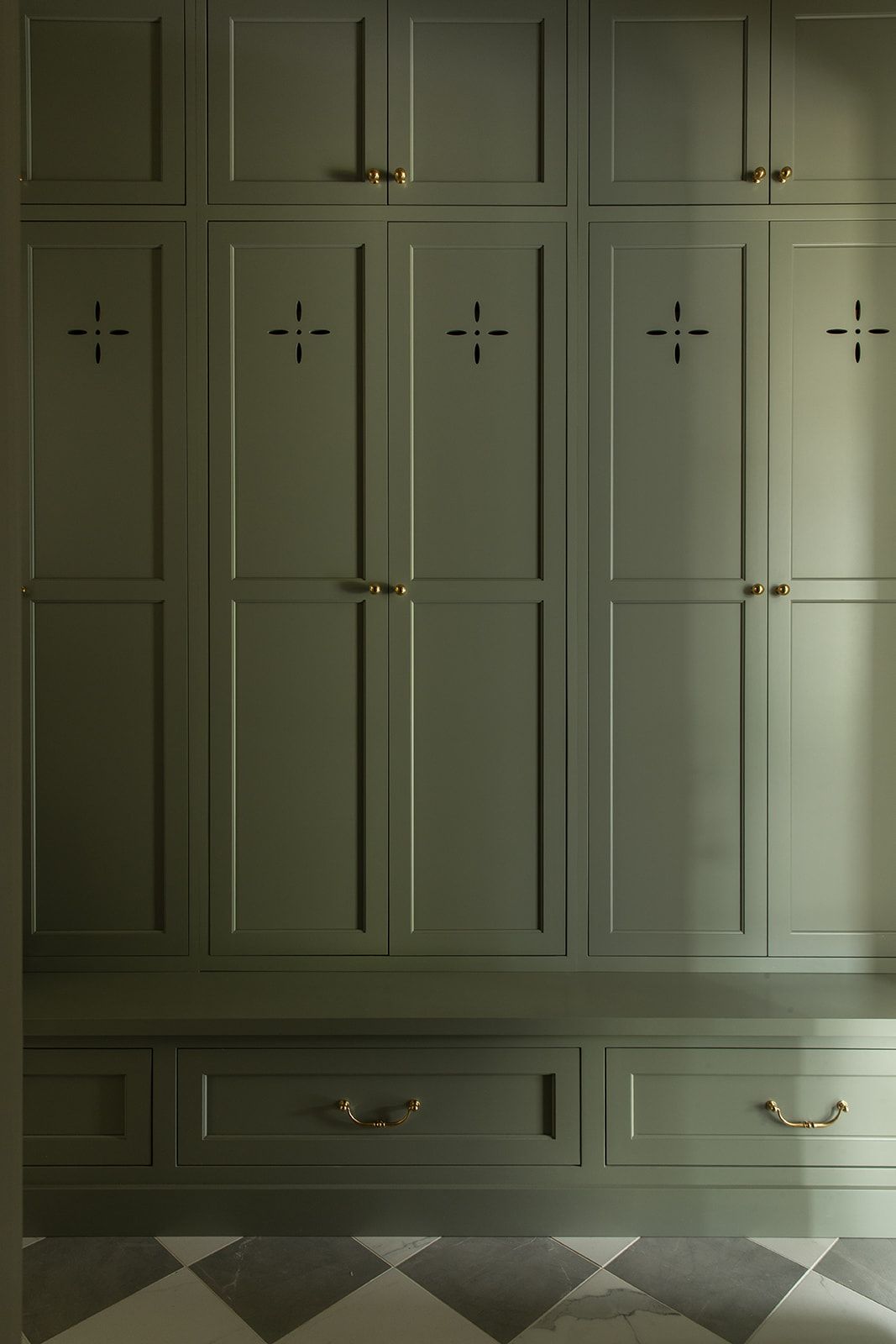 Olive green built-in wardrobes with brass handles and decorative cross details on a checkered floor.