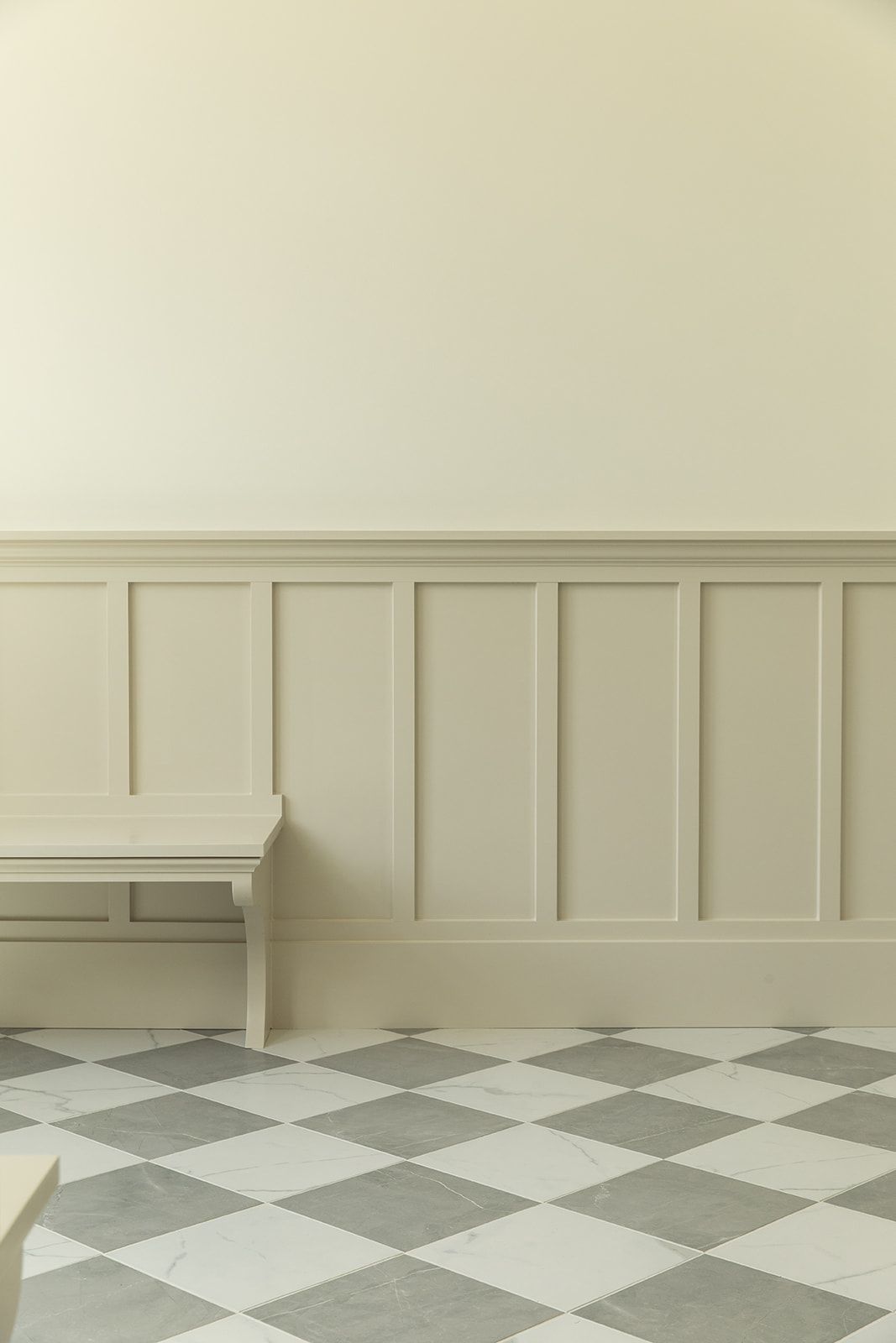 Sophisticated entryway with checkered marble floor, cream wainscoting panels, and minimalist bench against neutral walls.