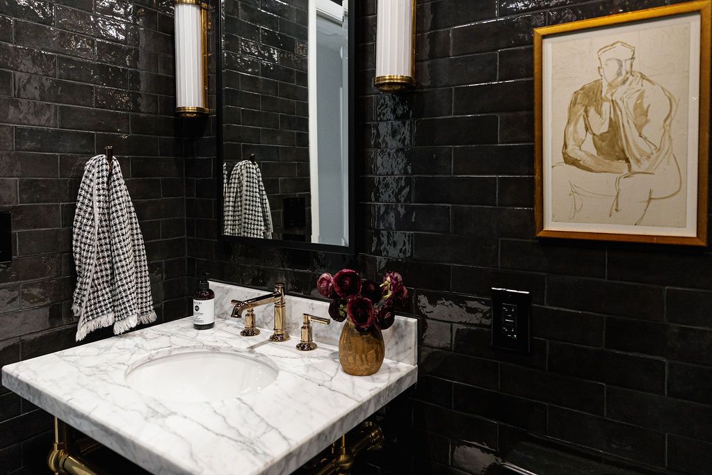 A modern bathroom with dark black tiles features white lighting fixtures and minimalist decor accents in gold and beige tones.
