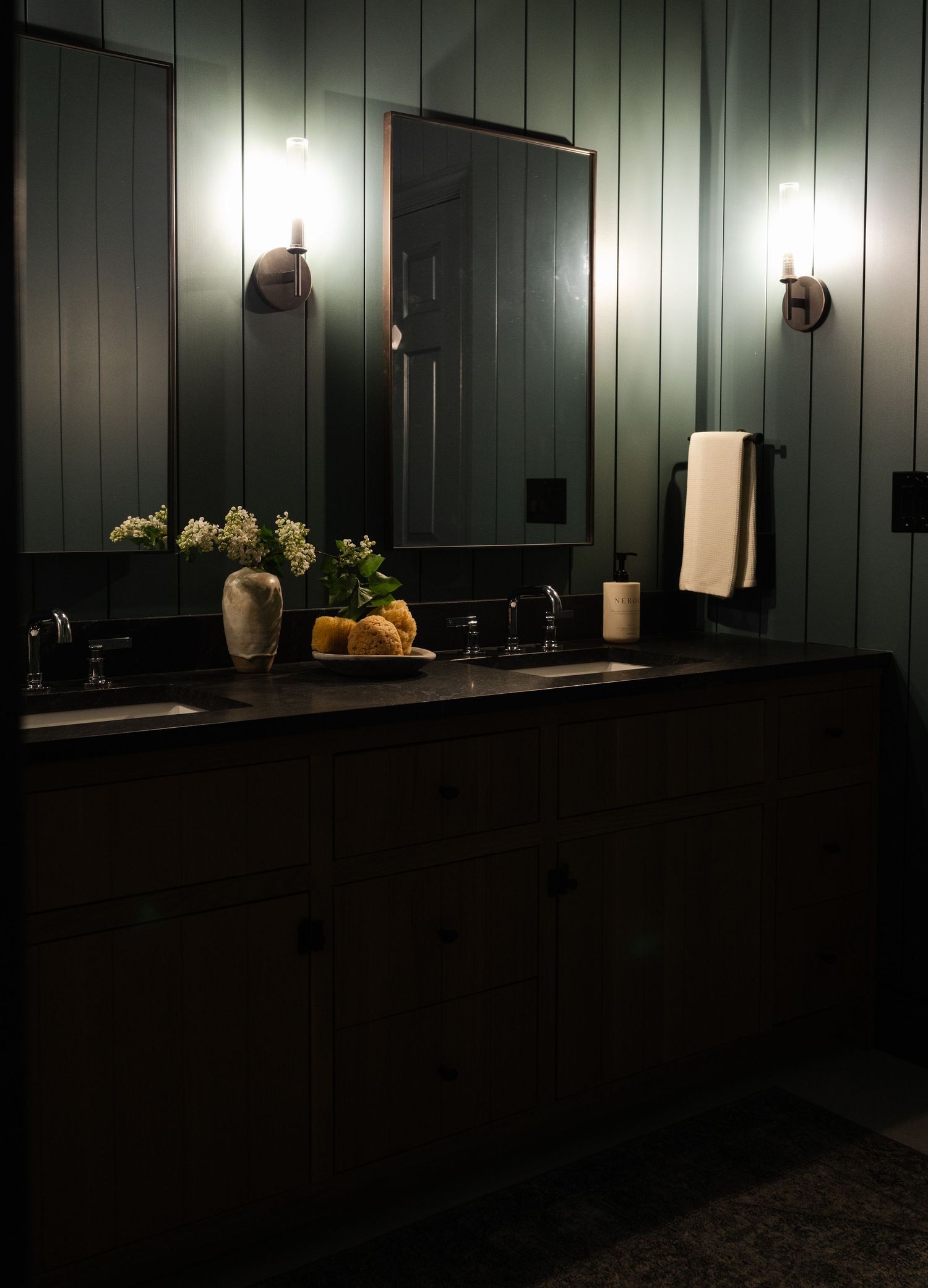 Modern bathroom interior with dark green walls, black vanity, decorative sconces, and elegant decor accents.