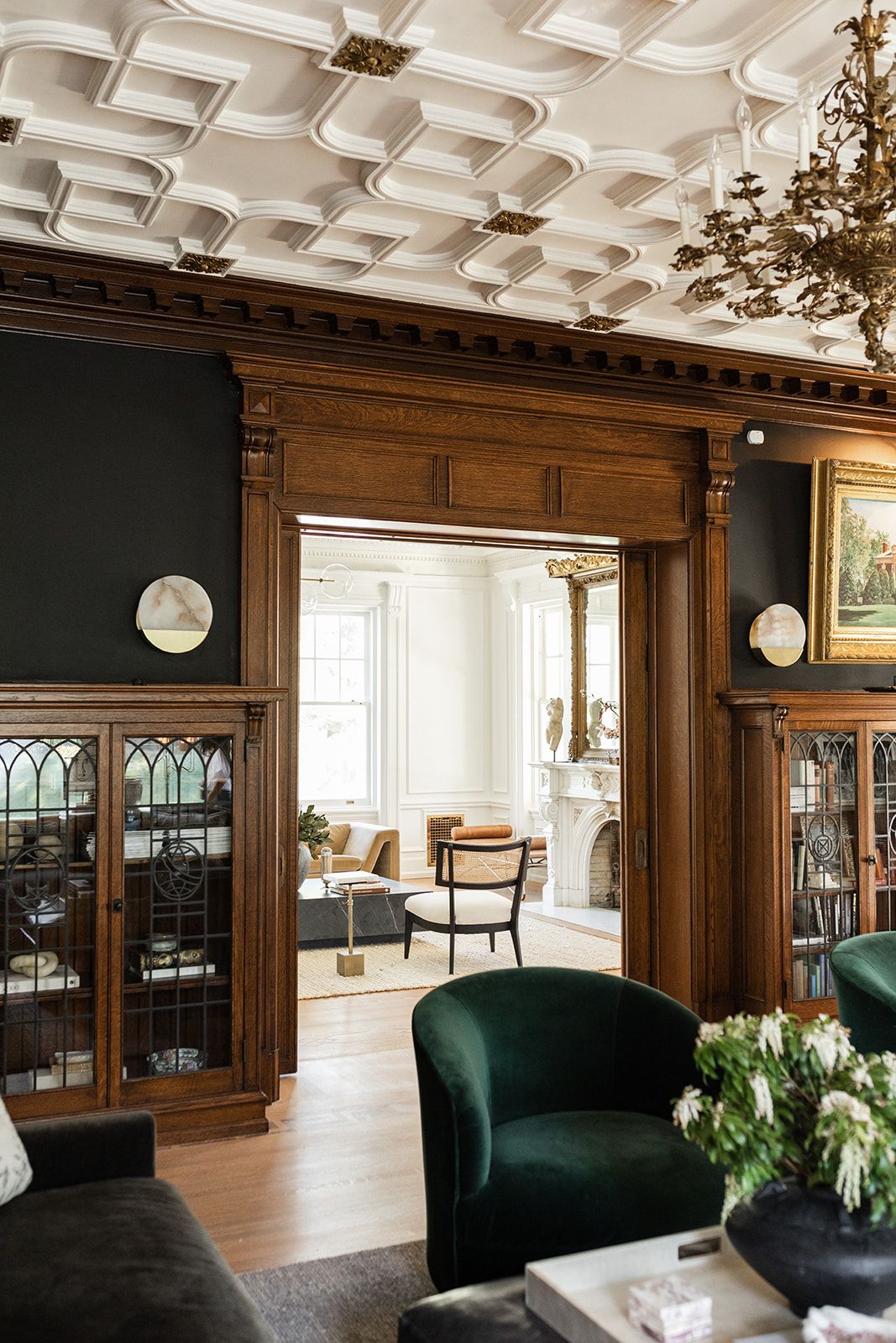 Luxurious living room with coffered ceiling, wood paneling, and emerald velvet chairs.