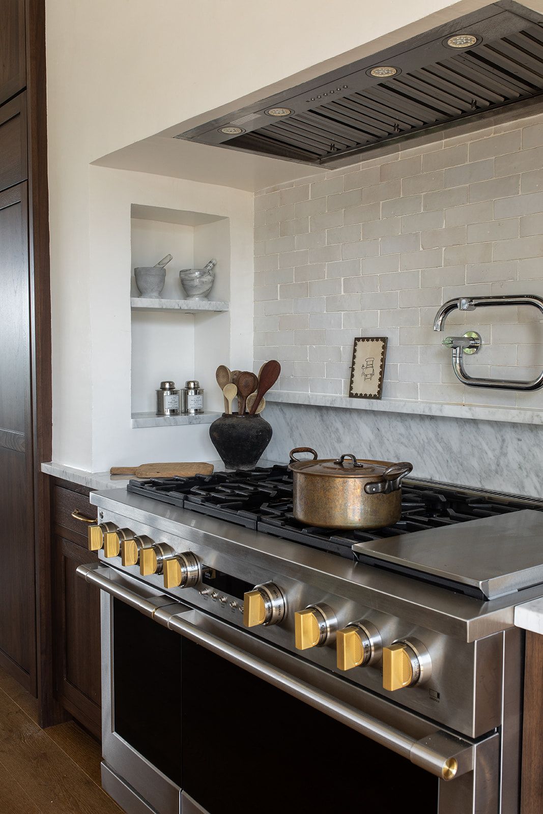 Professional stainless steel gas range with brass knobs, tile backsplash, and pot filler in luxury kitchen.