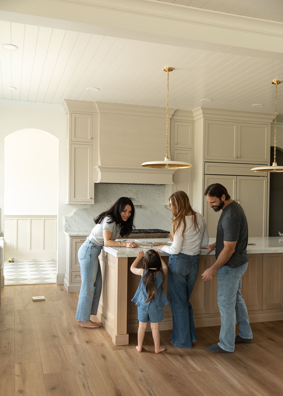 Family of four gathered around a kitchen island in a bright modern home with gold pendant lights.