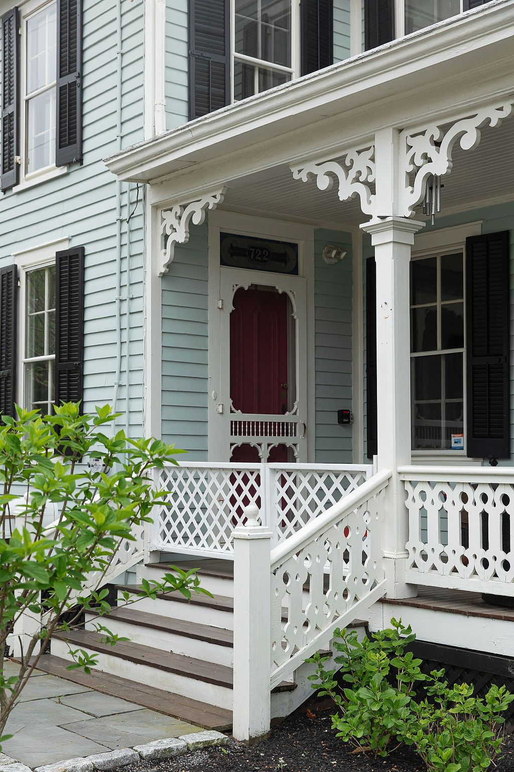 Elegant white porch with ornamental lattice railings and burgundy accents on a traditional Victorian home.