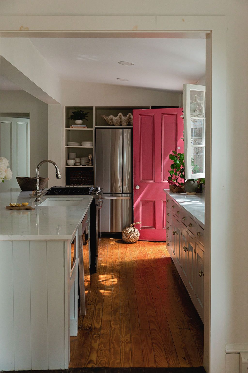 Modern kitchen with white cabinets, wood floors, and a striking pink door adding a pop of color.