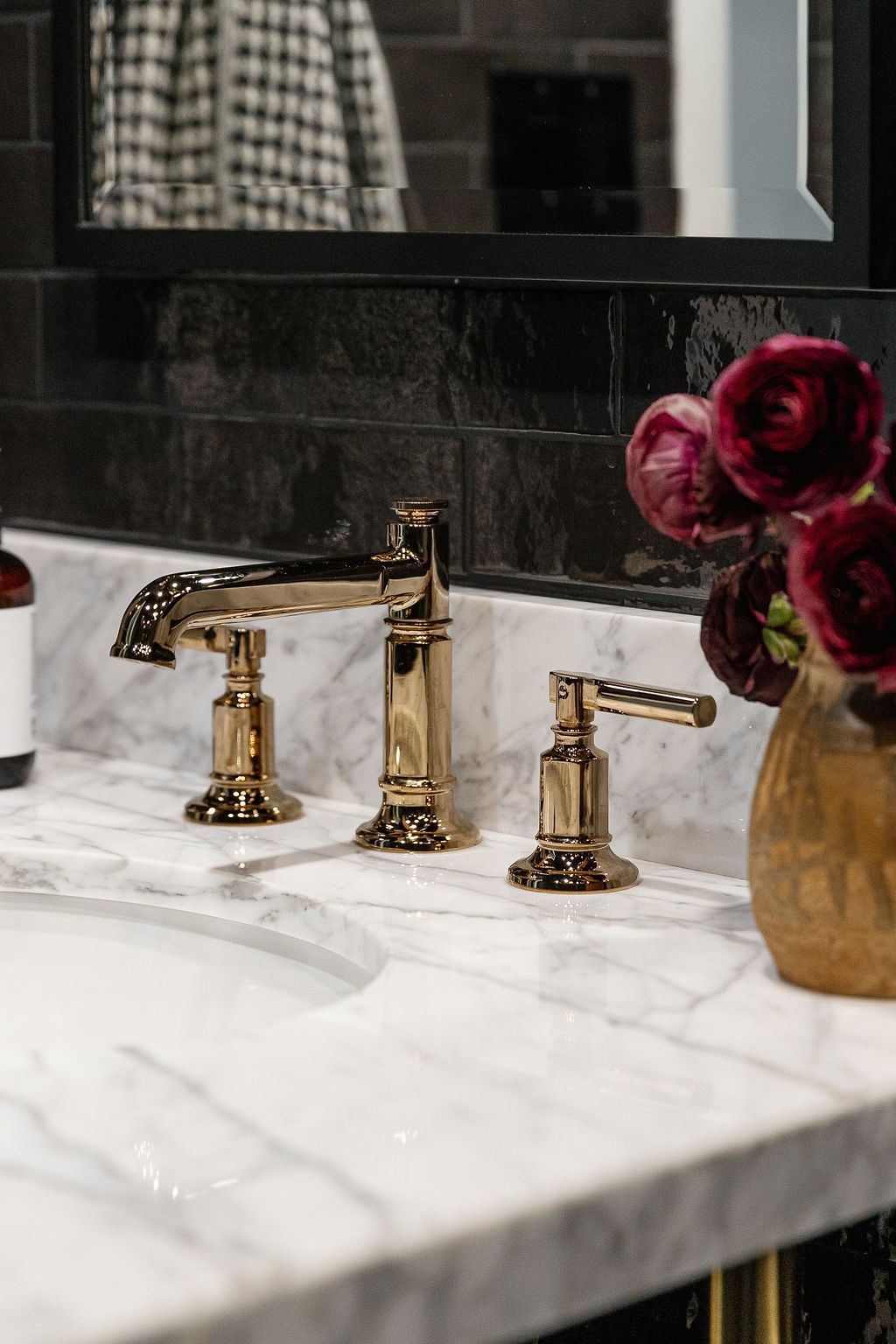 Gold brass faucets line up on white marble countertop against black tile wall with decorative burgundy flowers.