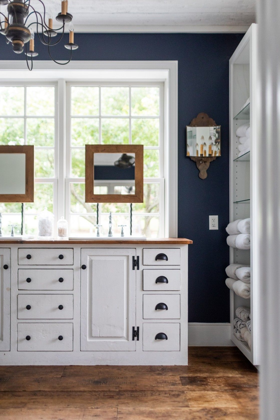 Navy blue and white farmhouse bathroom with wooden countertop vanity and built-in storage shelves near windows.