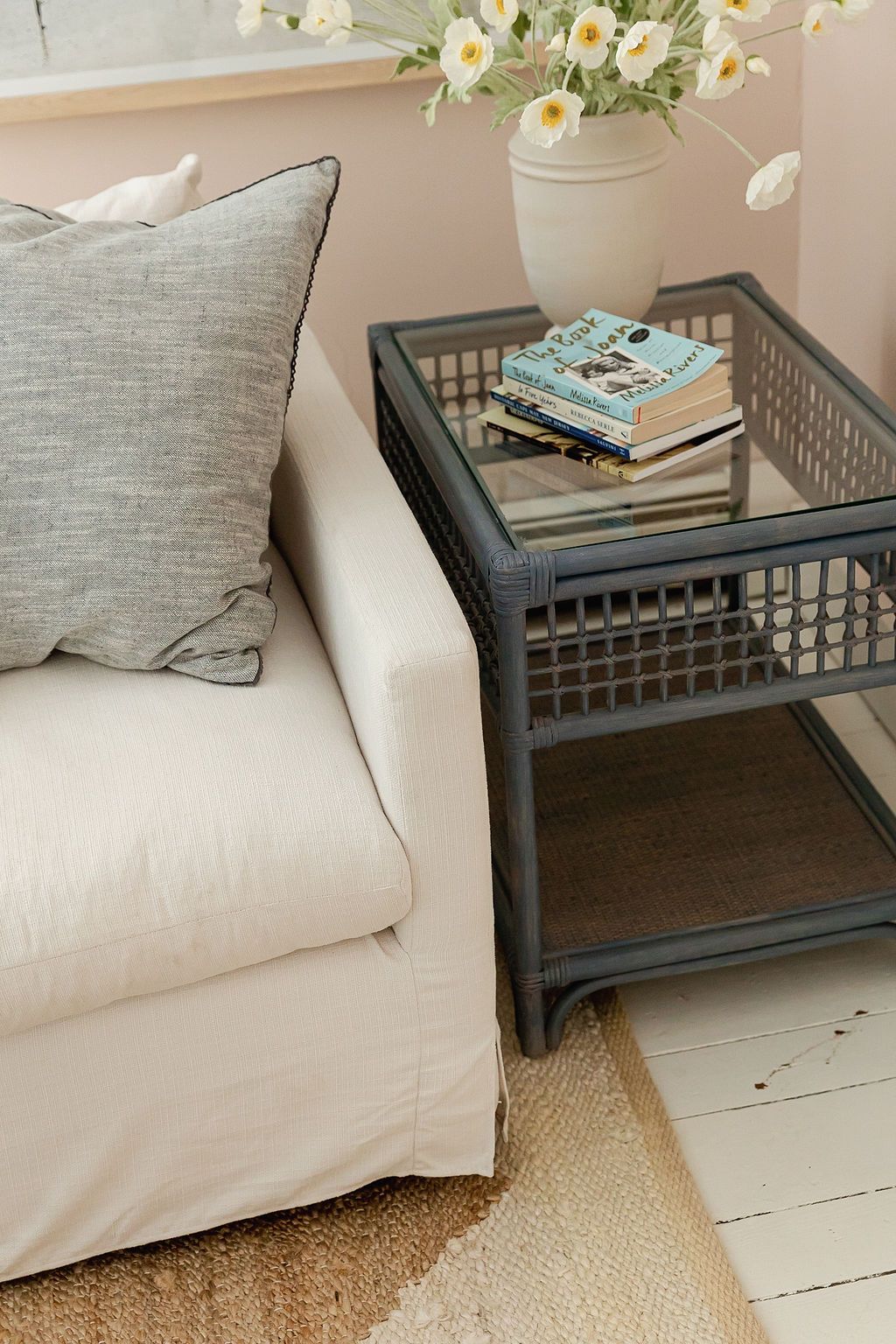 Close-up view of a gray sofa with white cushions beside a dark wood side table on painted white floorboards.