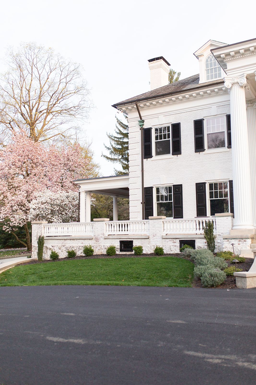Stately white mansion with black shutters and blooming cherry trees in springtime.