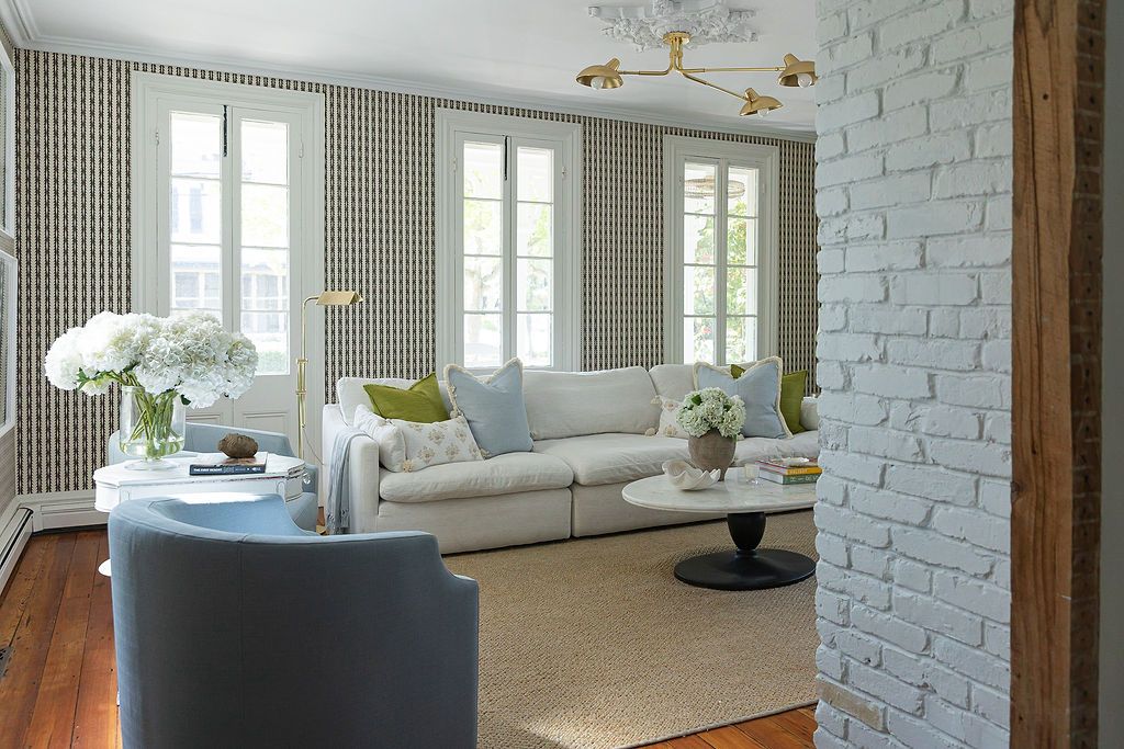 Modern living room with white painted brick wall, grey sofa, patterned wallpaper and hardwood floors.