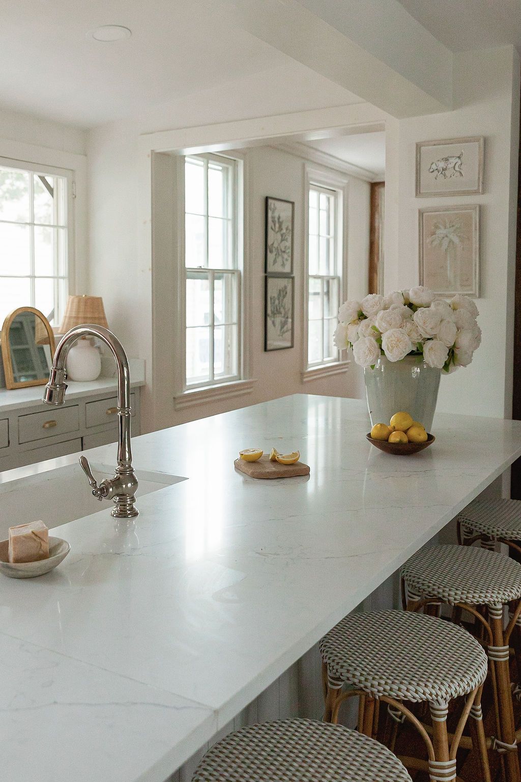 Elegant white kitchen counter with vintage faucet, white flowers in vase, and bistro-style seating.