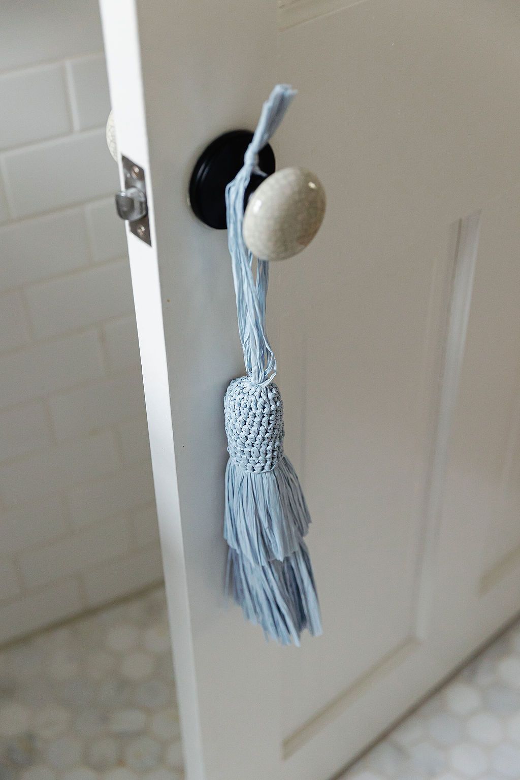 A light blue decorative tassel hangs from a white door handle against a white bathroom door.