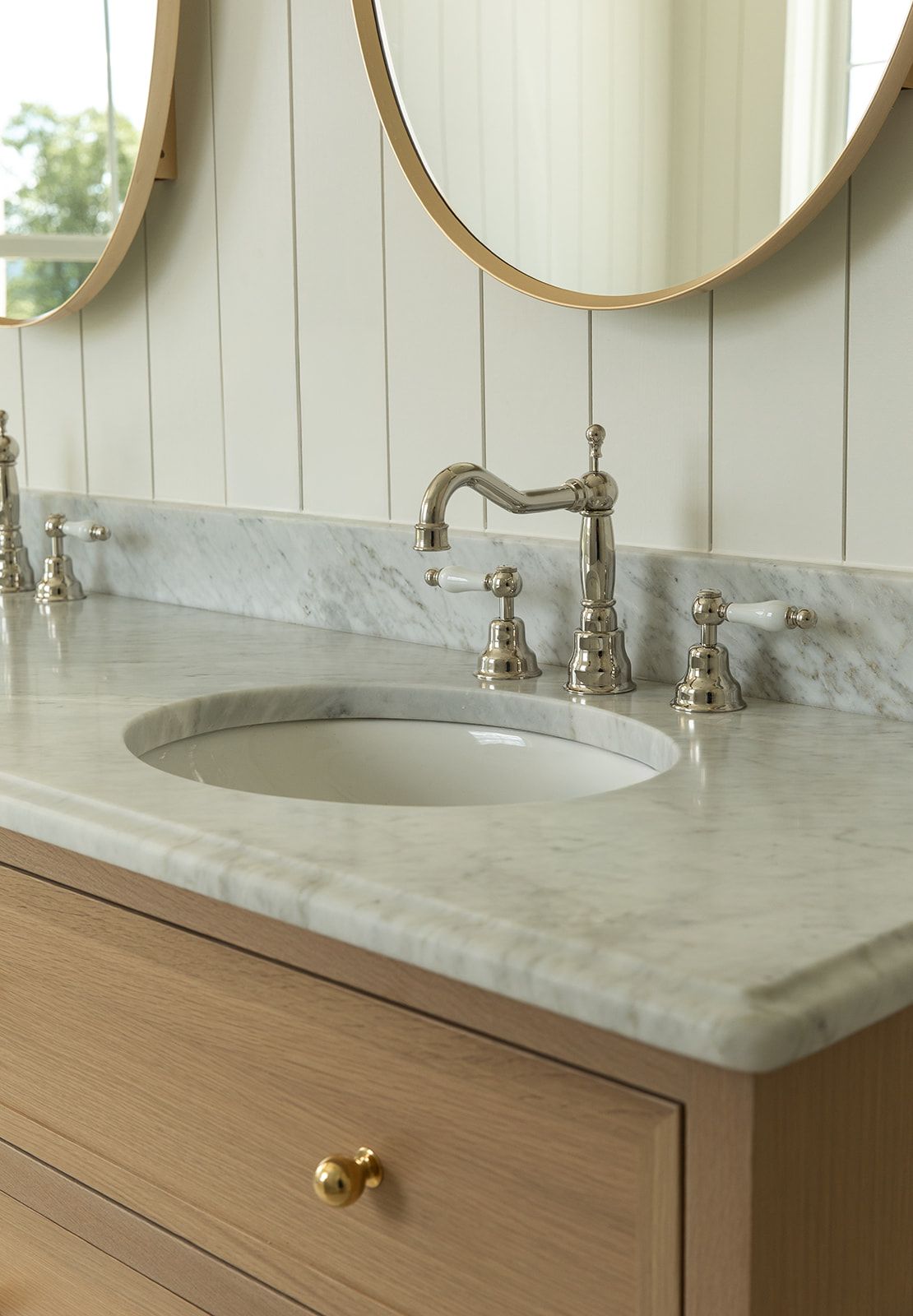 Elegant bathroom vanity with marble countertop, polished nickel faucet, undermount sink, wood cabinet, and round gold mirrors.