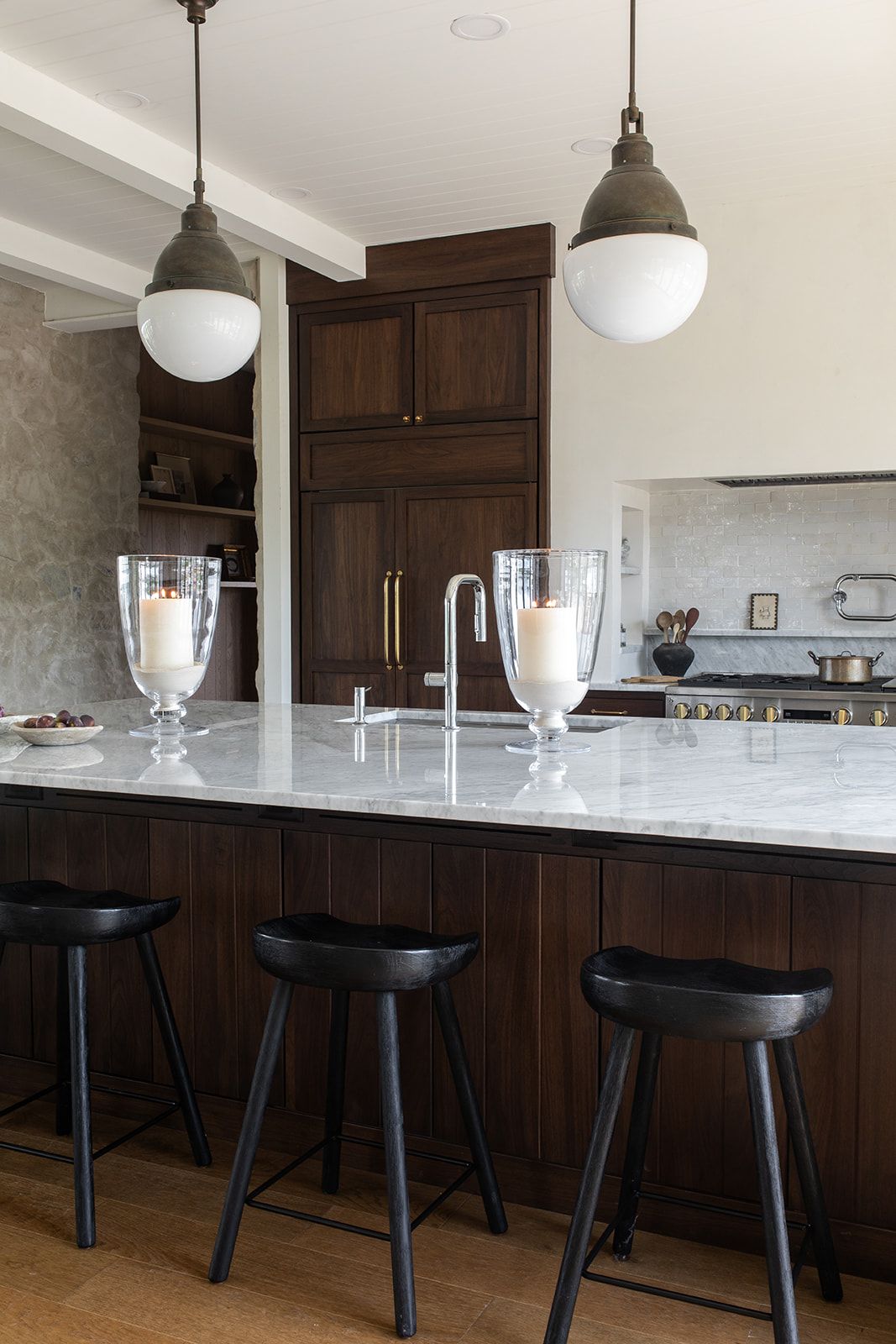 Dark walnut kitchen island with white marble countertop, black bar stools, and globe pendant lights.