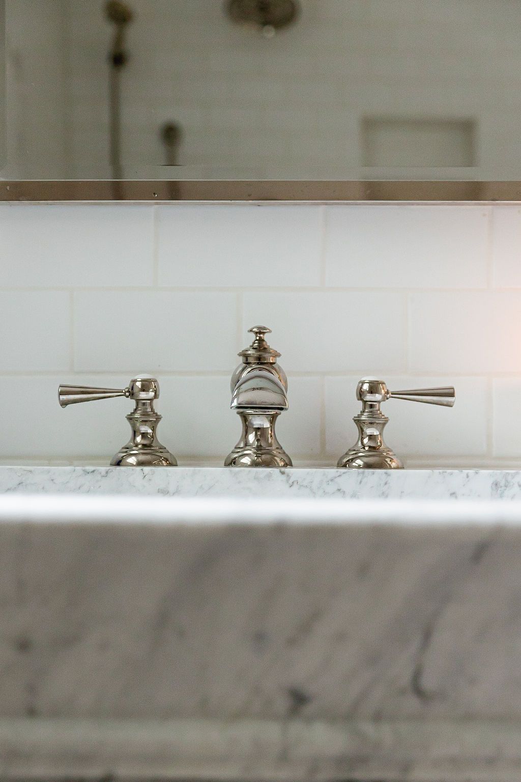 Close-up view of polished nickel bathroom faucet handles and spout on white marble counter.