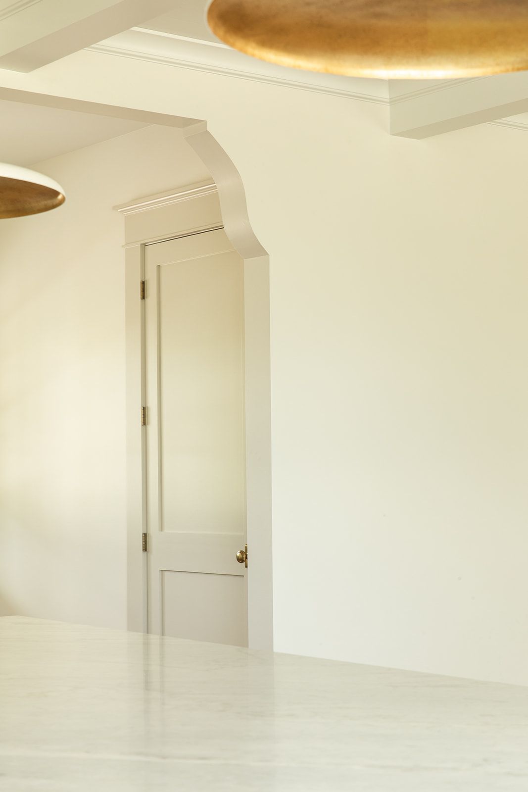 Bright minimalist dining room with white marble floors, arched doorway, white walls, and gold circular pendant lights.