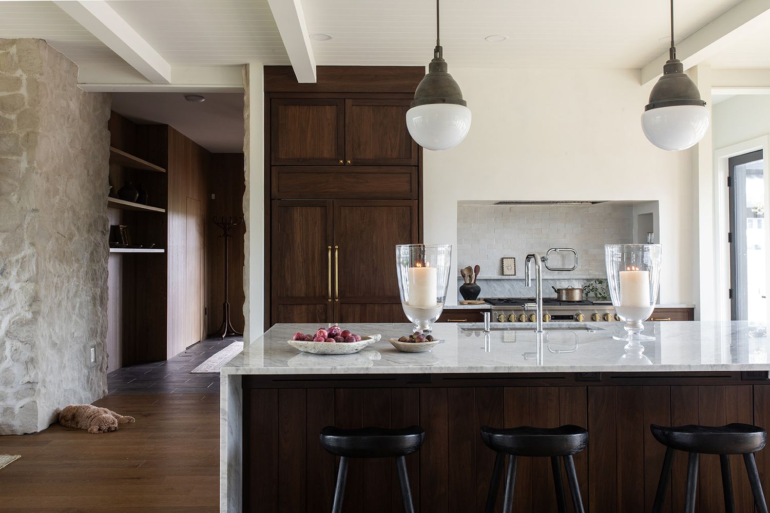 Modern kitchen with dark walnut cabinets, marble island, black bar stools, and globe pendant lights on hardwood floors.