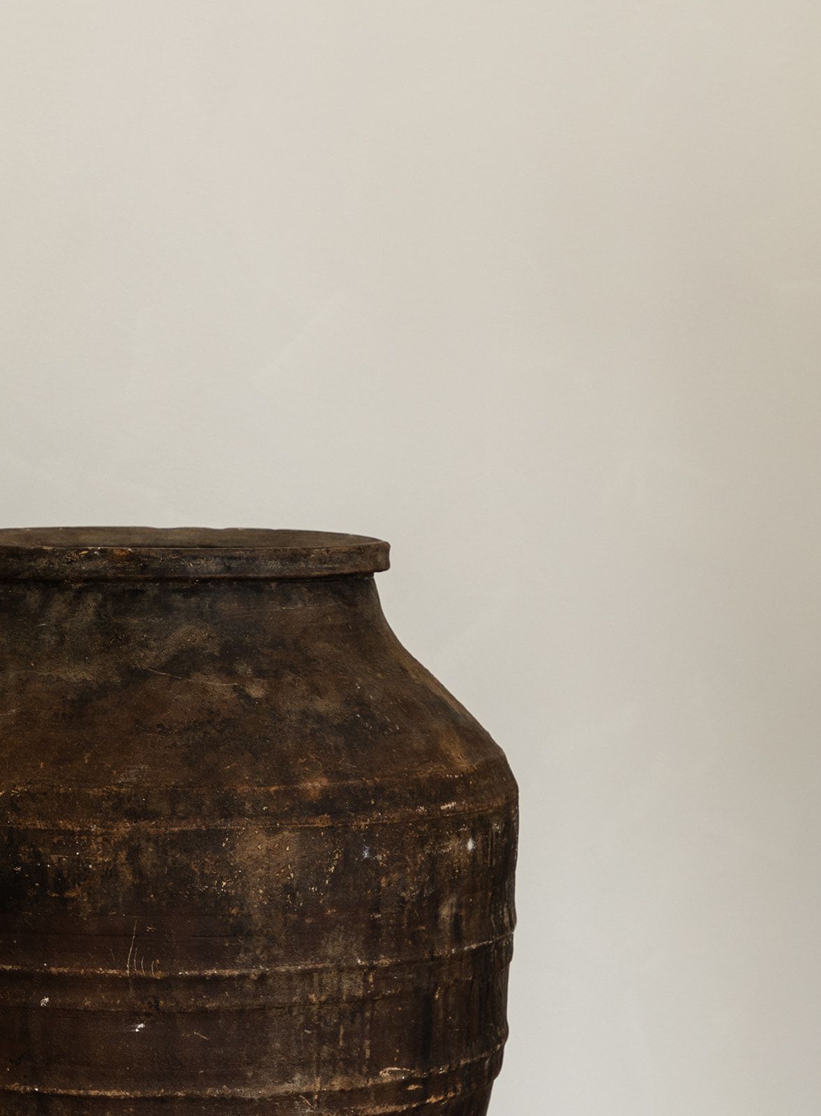 Close-up view of a rustic brown clay pot or urn against a light neutral wall.
