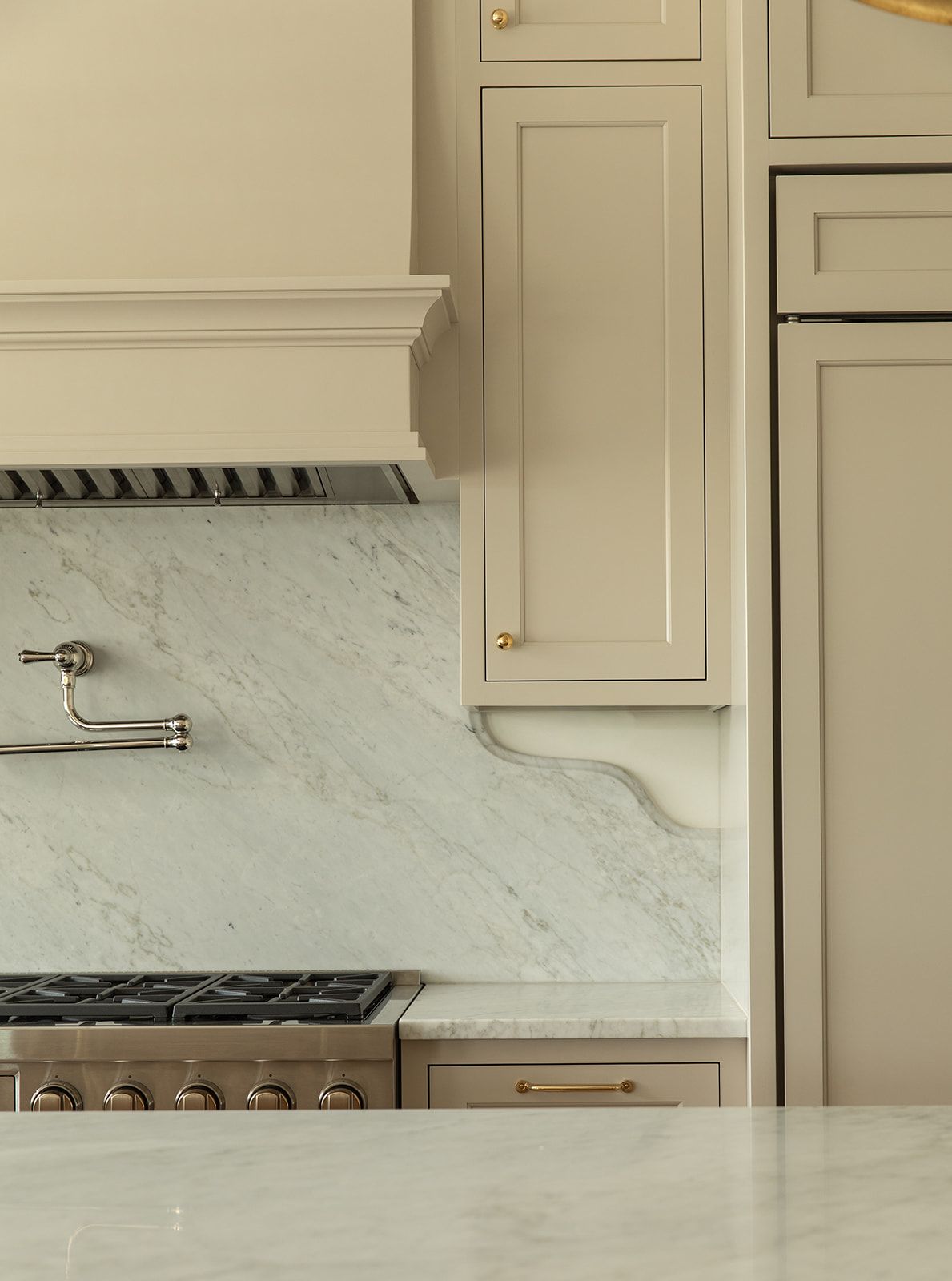 Elegant kitchen with sage green cabinets, marble backsplash, brass hardware, and professional stainless steel range with pot filler.