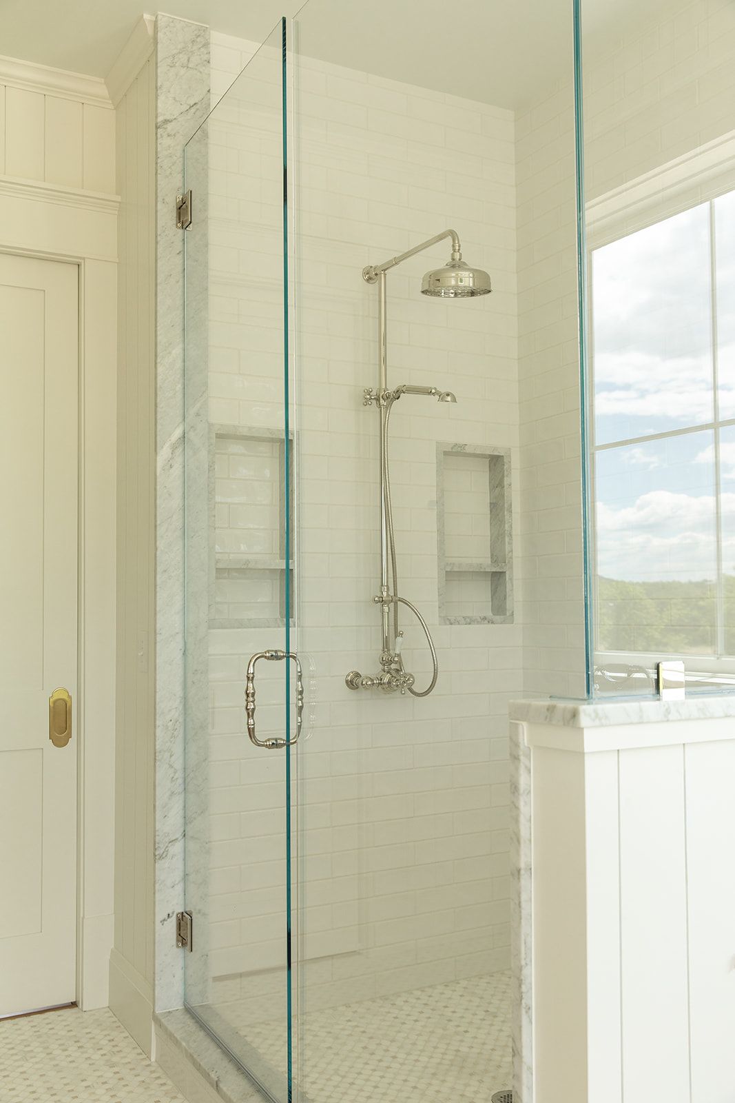 Elegant glass-enclosed walk-in shower with rainfall showerhead, white subway tiles, marble accents, and built-in niches.