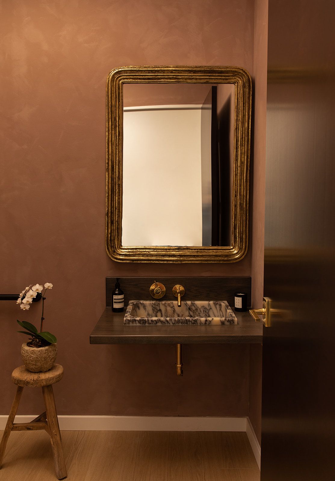 Elegant bathroom vanity with gold-framed mirror and orchid plant on wooden stool.