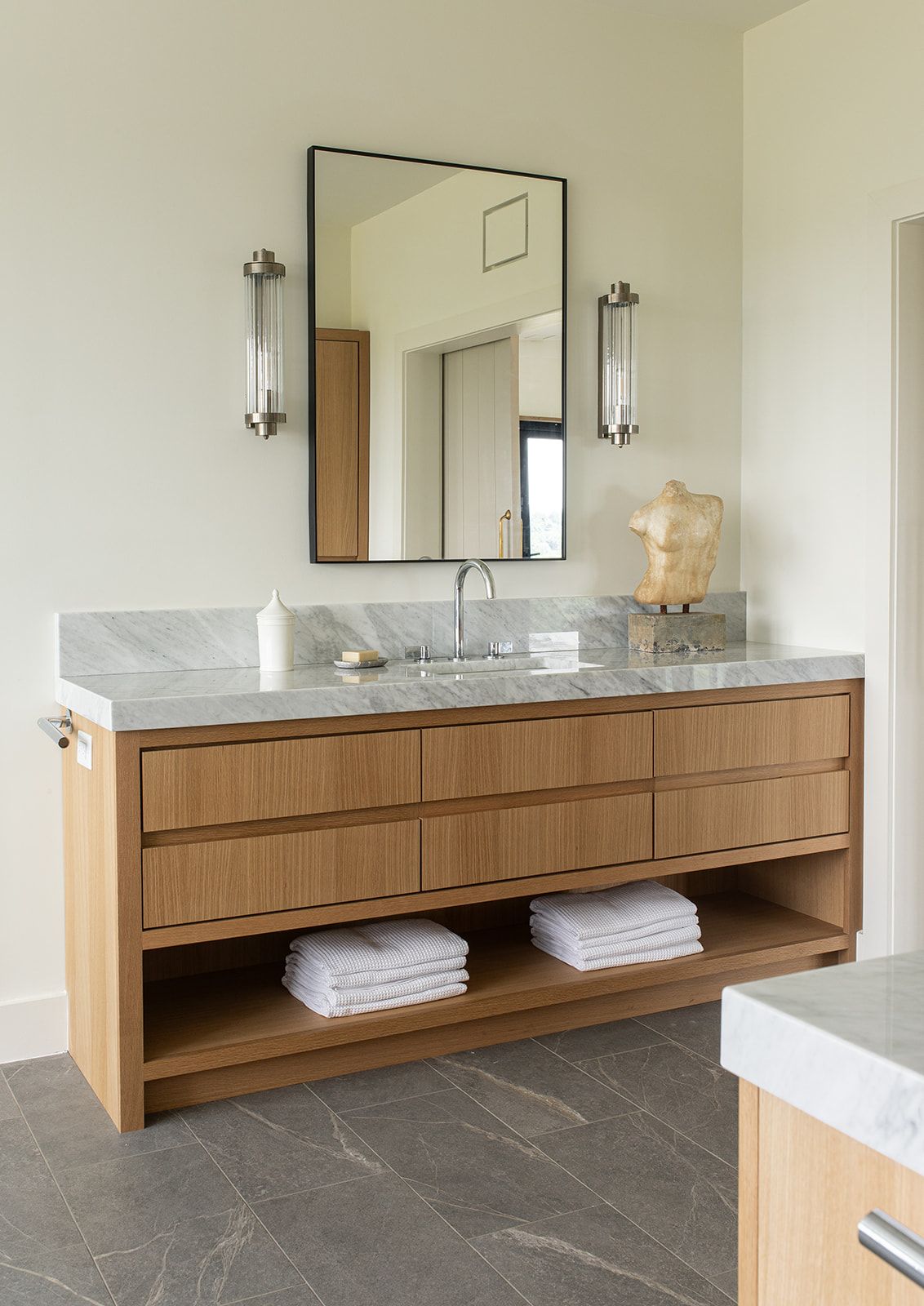 Floating wood bathroom vanity with marble countertop, black framed mirror, and crystal wall sconces.