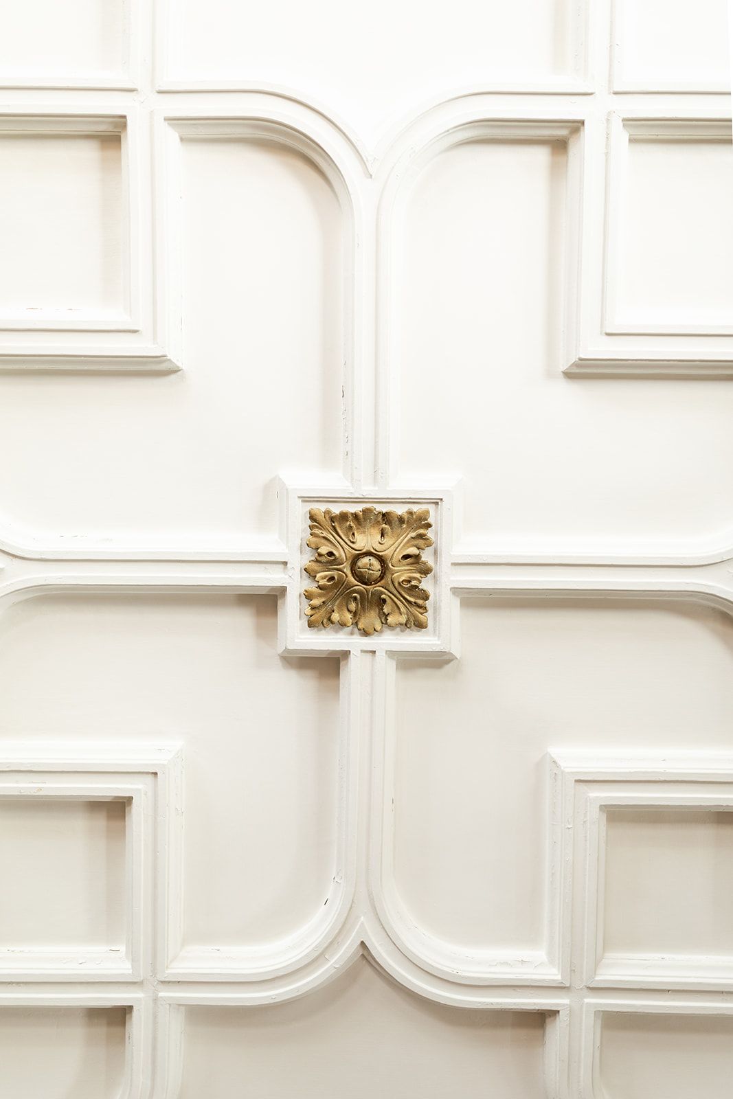 Ornate white decorative wall panel with golden floral accent detail at the center intersection.