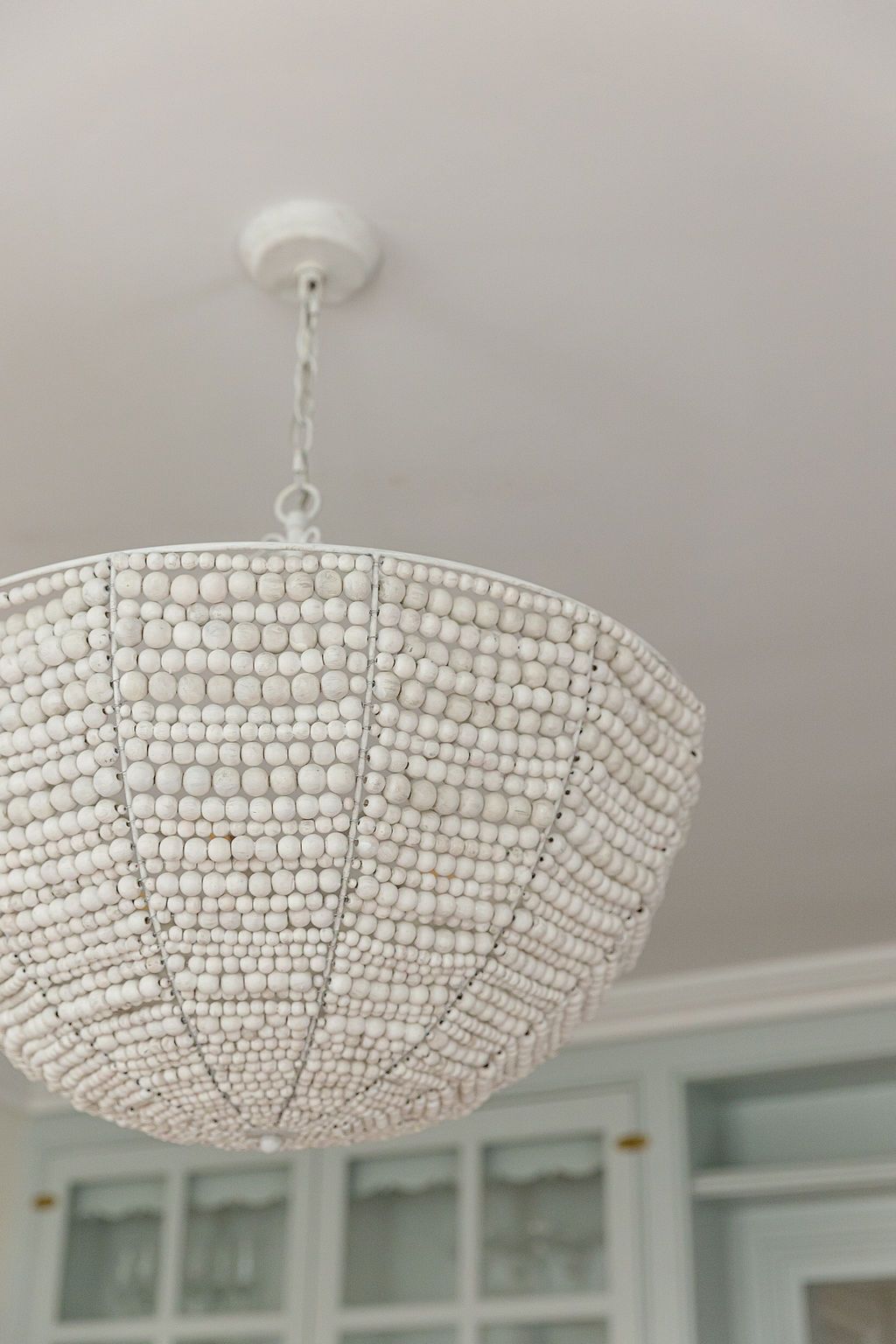 A white beaded dome chandelier with crystal details hangs from a ceiling, creating an elegant lighting fixture.