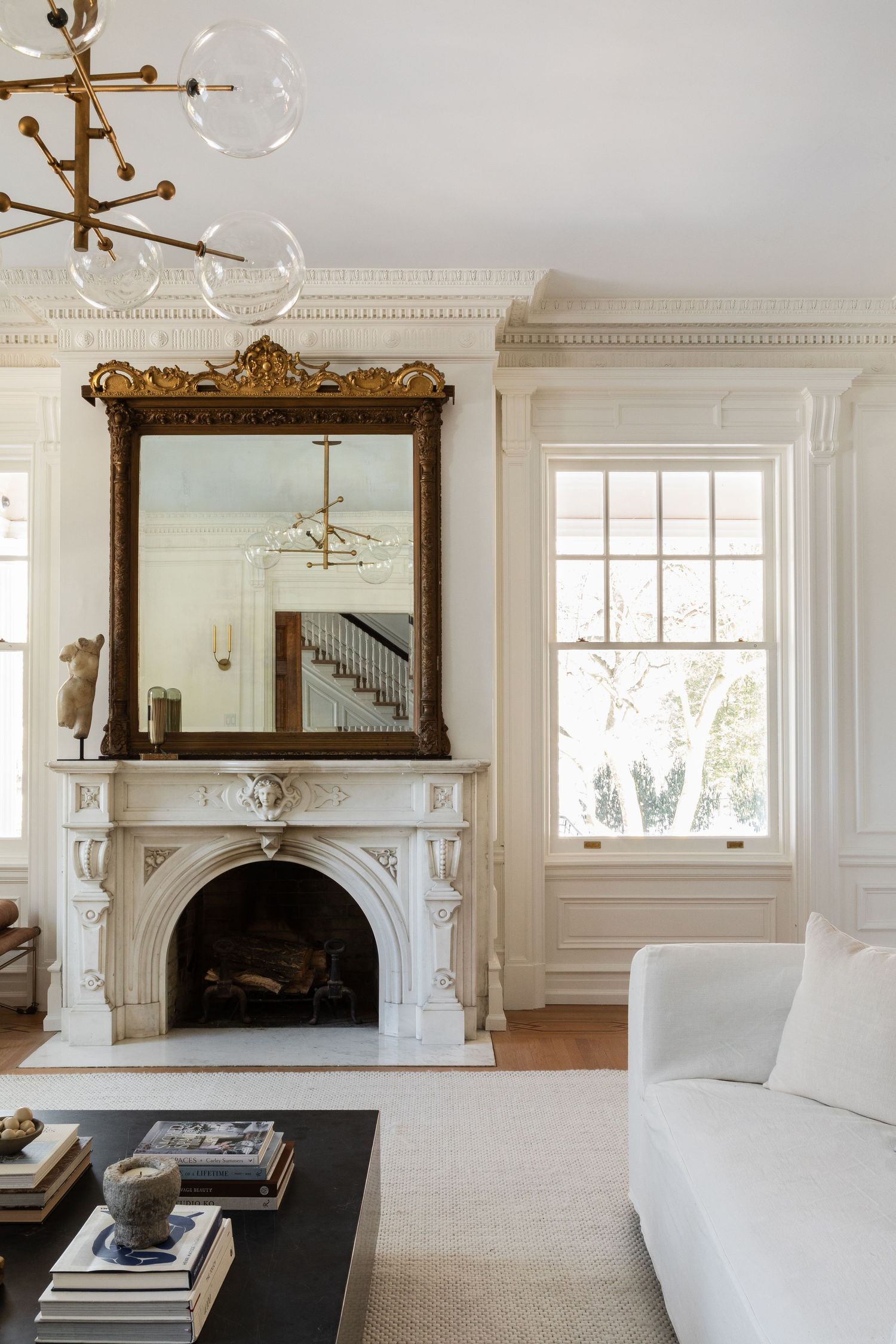 Elegant living room with marble fireplace, ornate gold mirror, and modern white furniture.