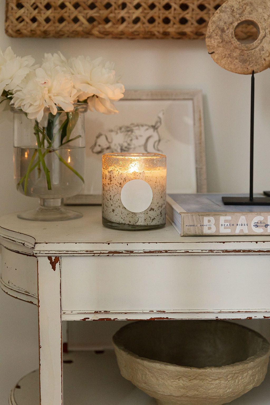 A rustic white painted shelf displays decorative items including candle holders, vases with flowers, and glass jars.
