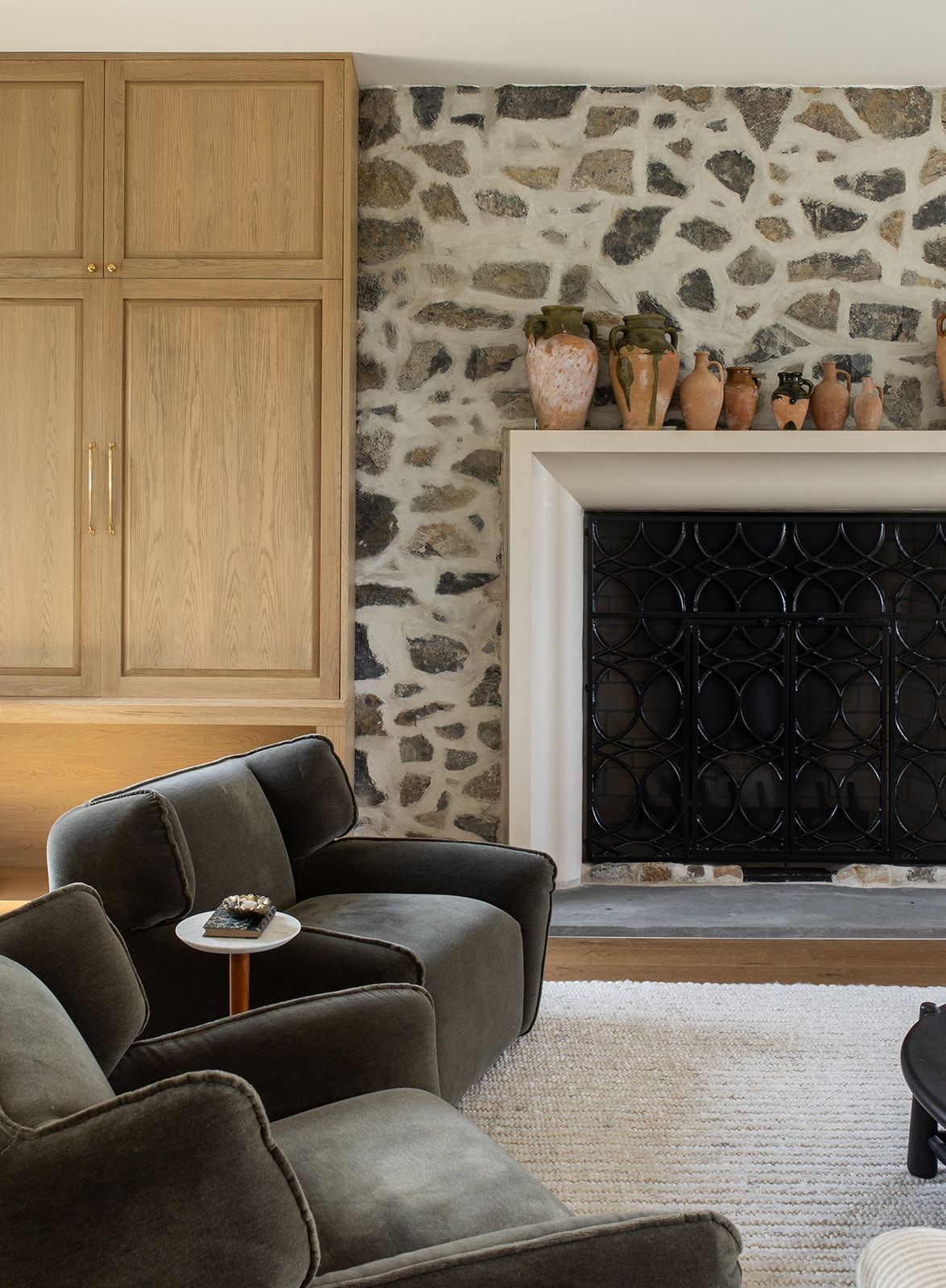 Cozy living room with stone fireplace, dark velvet chairs, wood built-ins, and terra cotta pots on mantel.