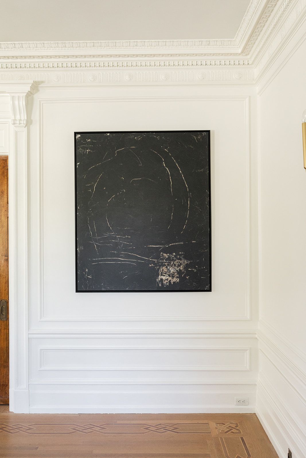 Abstract black artwork mounted on white wall with detailed crown molding.