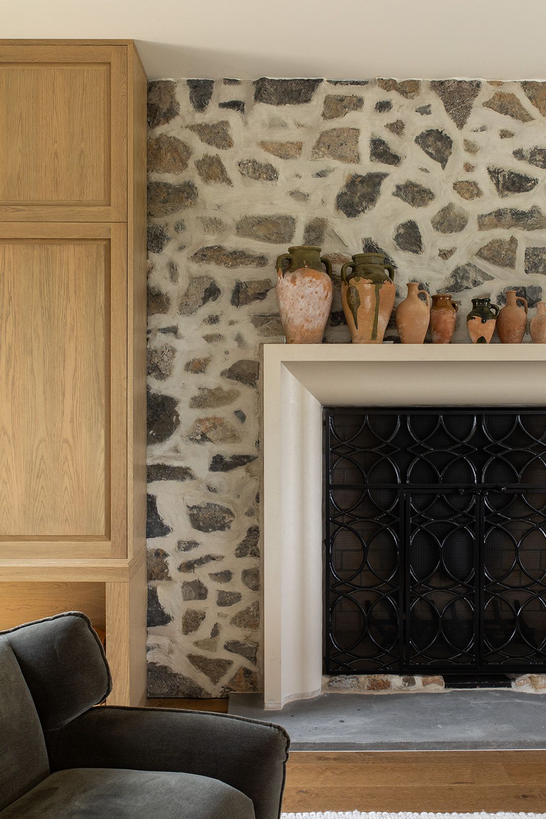 Stone fireplace with white surround, decorative ceramic vases on mantel, wood cabinetry, and dark geometric firebox screen.