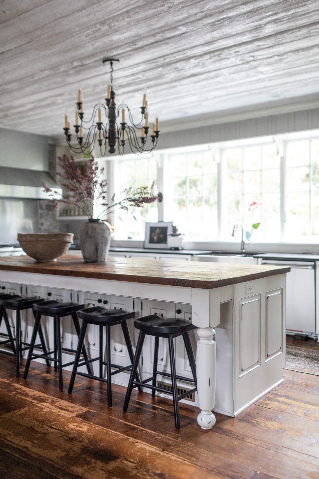 Modern farmhouse kitchen with white island, butcher block countertop, black bar stools and elegant chandelier.