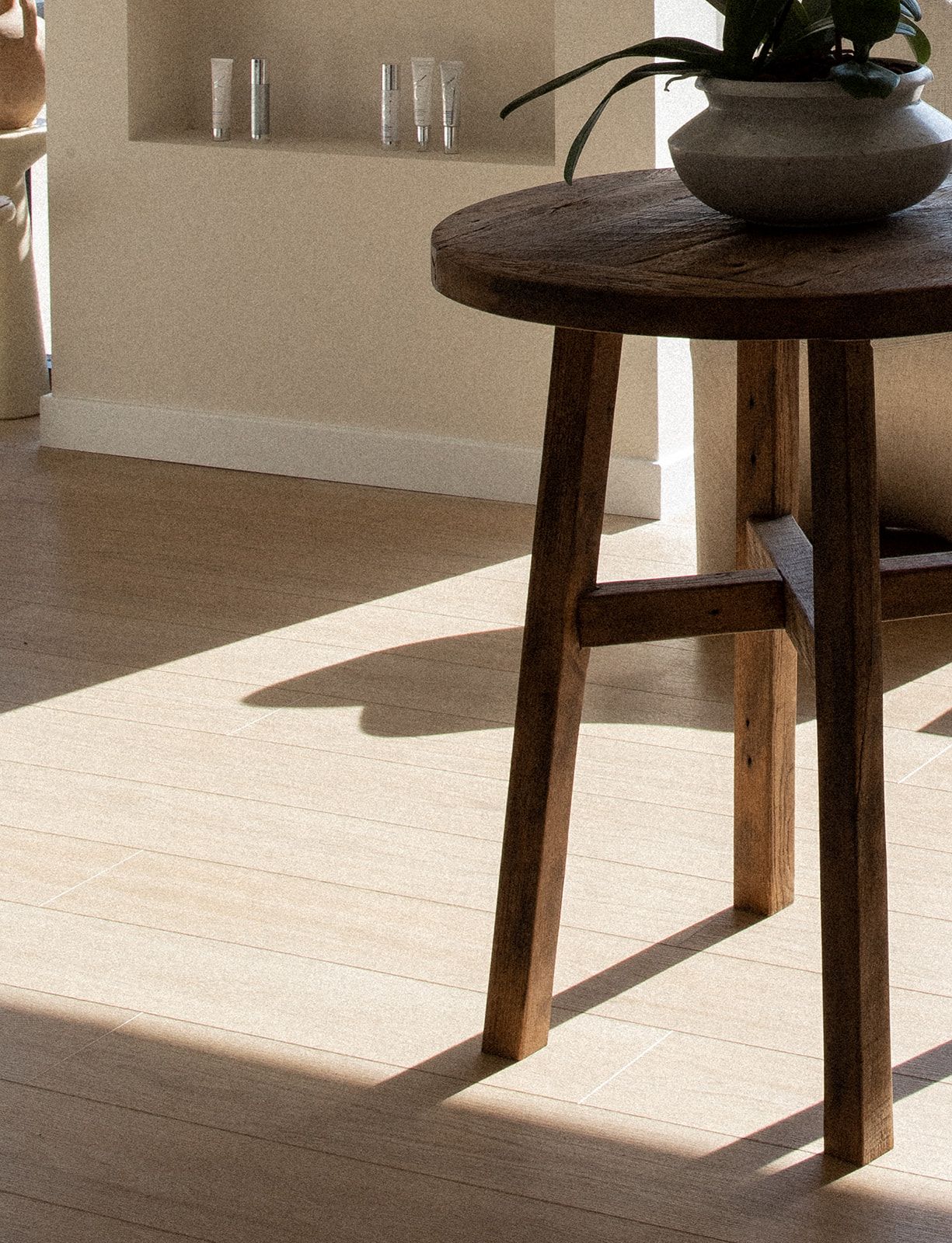 Wooden side table with a dark stained finish casting dramatic shadows on a light wooden floor in a minimalist setting.