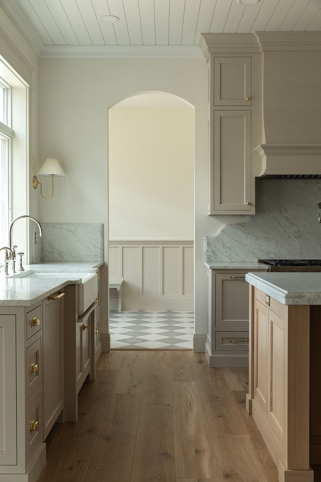 Elegant kitchen with taupe cabinets, marble countertops, brass hardware, arched doorway, and white oak hardwood floors.