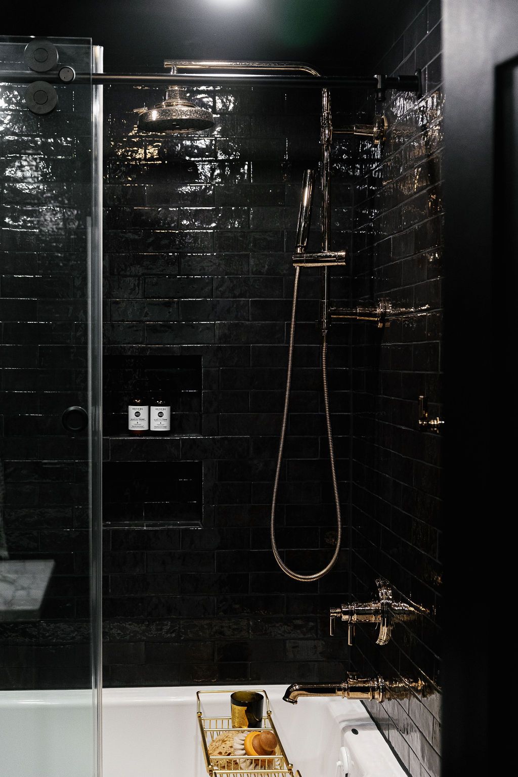 Sleek modern bathroom with black marble tiles, brass fixtures and chrome shower head in minimalist design.