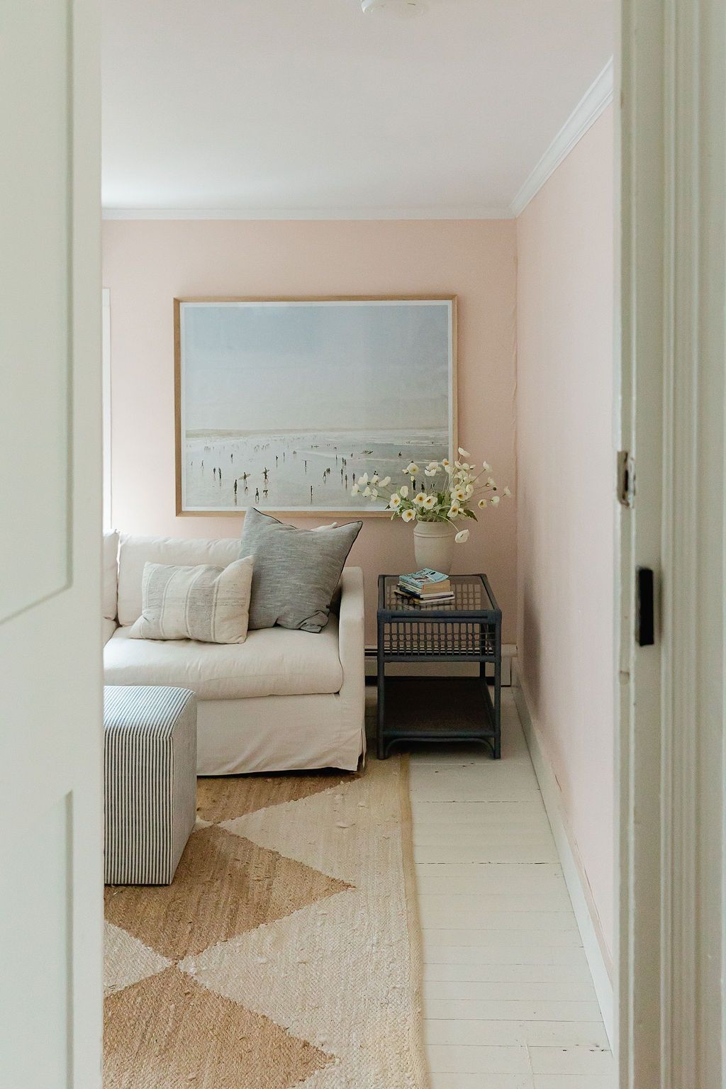 A cozy living room corner with a white sofa, beach artwork, and geometric patterned area rug.