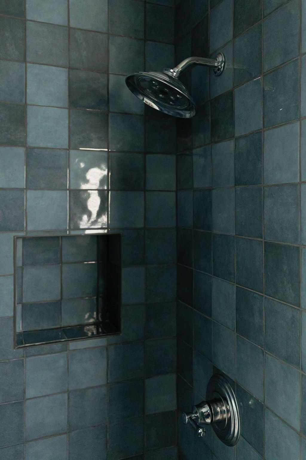 Dark teal tiled bathroom walls with chrome shower fixtures and recessed lighting create a modern, sleek atmosphere.