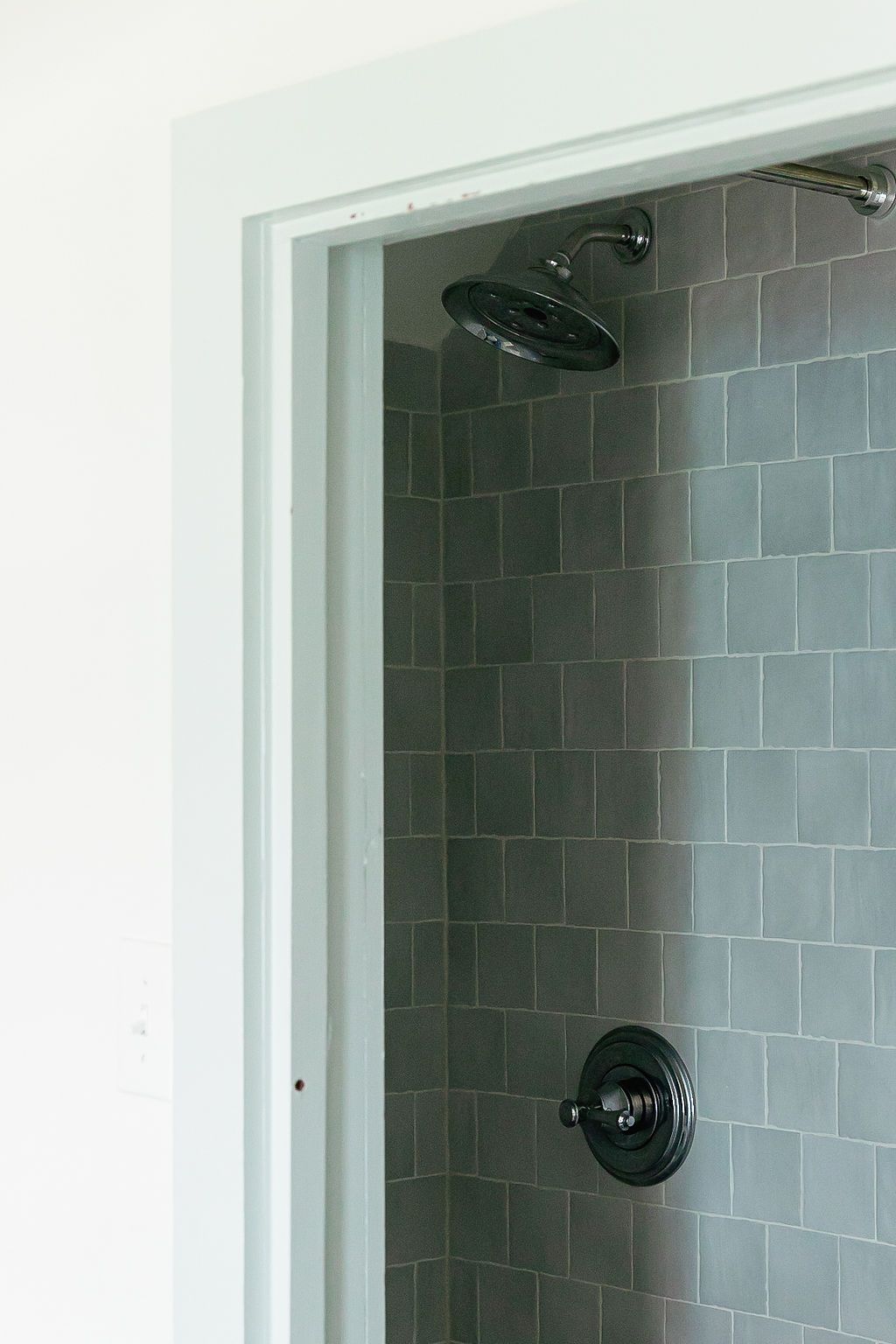 Modern bathroom shower stall with light gray subway tile and dark bronze fixtures mounted on white walls.