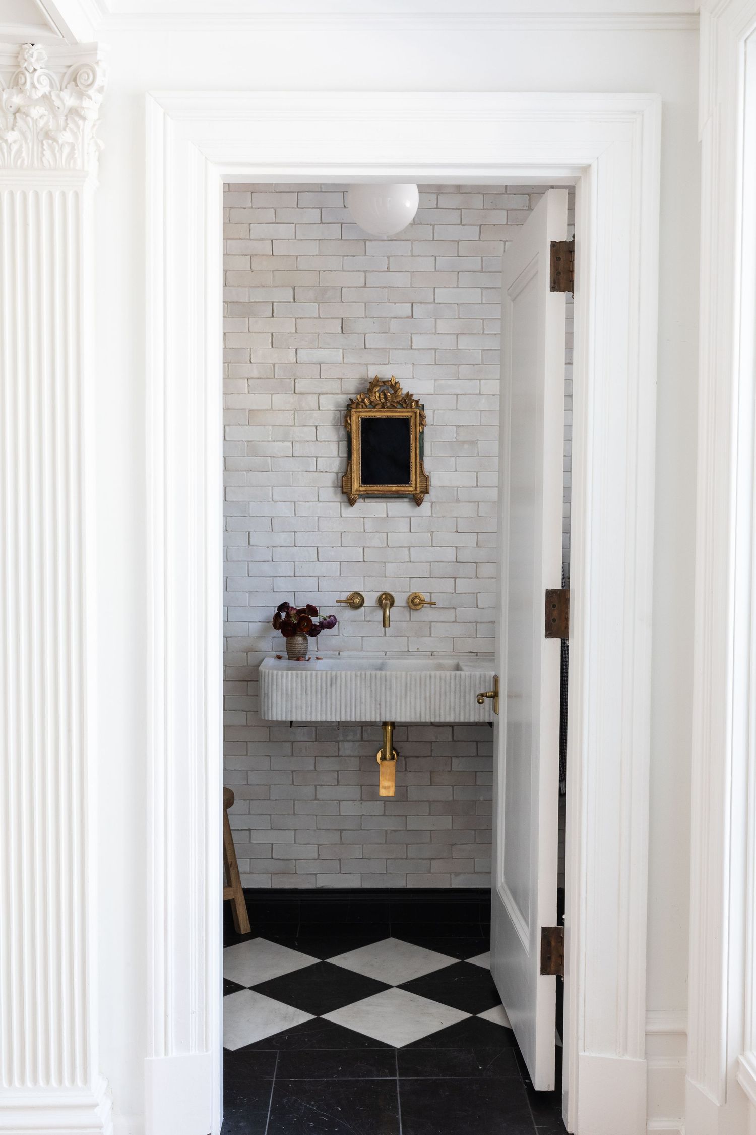Modern powder room with white brick walls, checkered floor, and vintage gold mirror.