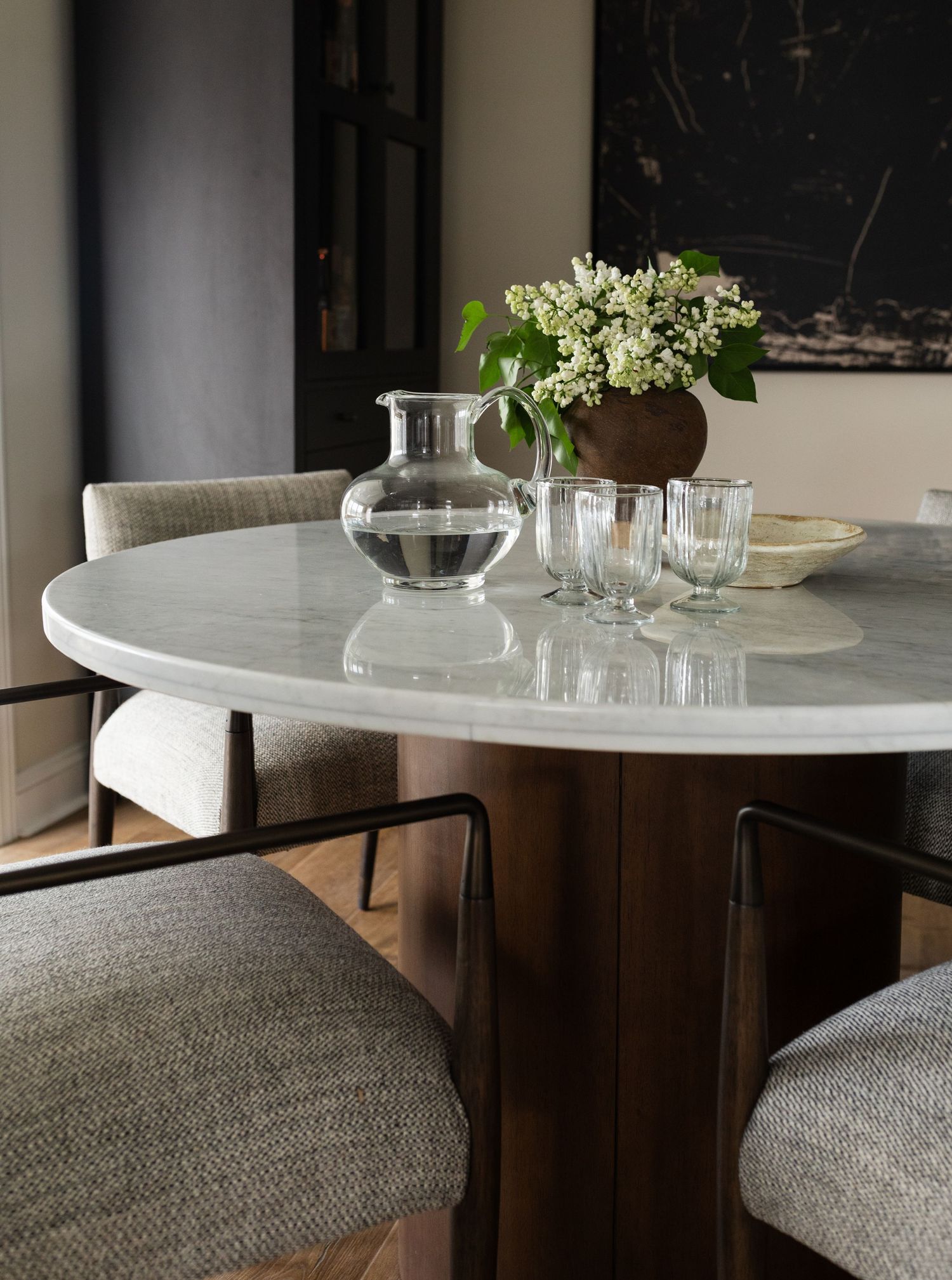 Elegant dining space with round marble table, grey upholstered seating and glass vase centerpiece.