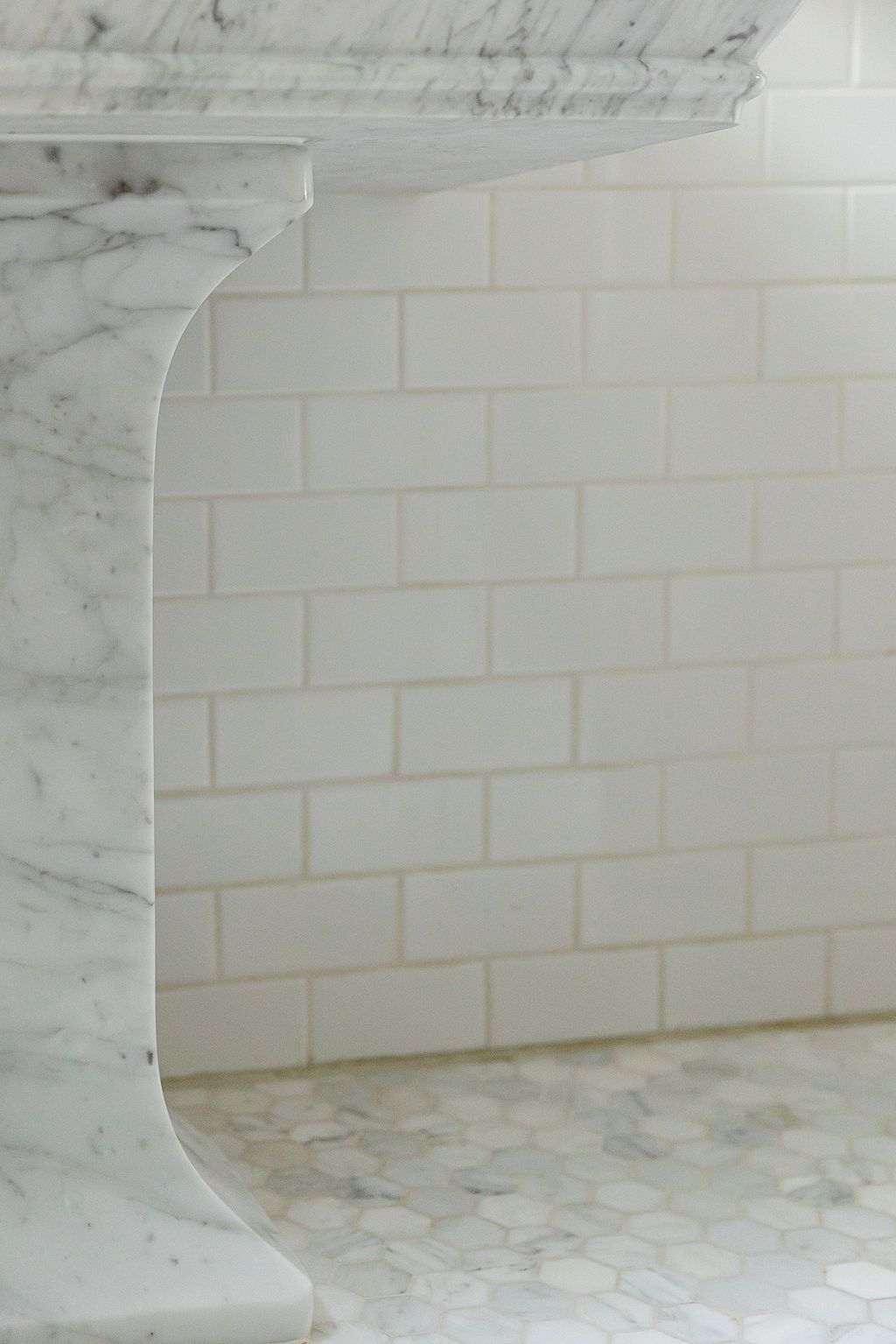 Detail of white marble bathroom featuring a curved wall edge with subway tile backsplash and polished stone surfaces.