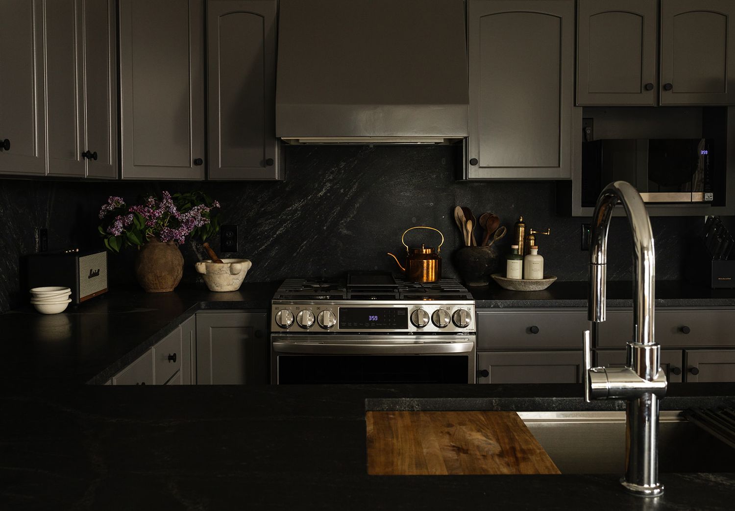 Modern kitchen interior features white cabinets, stainless steel appliances, and dark countertops under ambient lighting.
