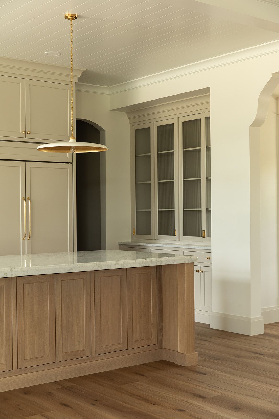 Transitional kitchen with natural wood island, cream upper cabinets, glass-front display cabinets, and gold pendant light.