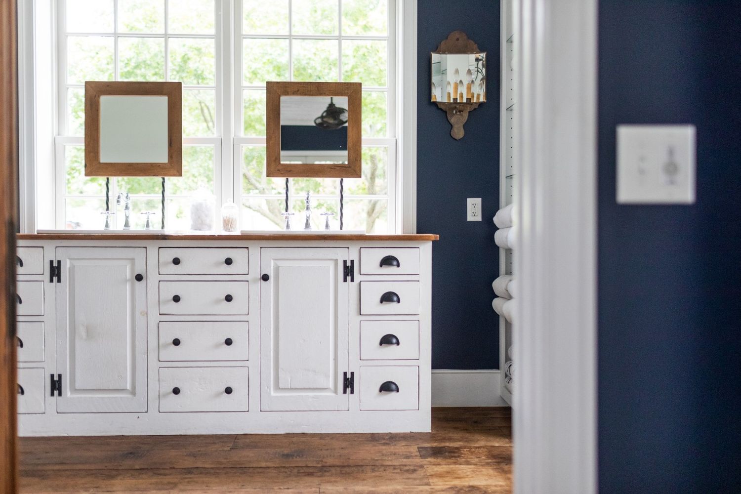 White vanity cabinet with black hardware against navy walls and two framed mirrors above.