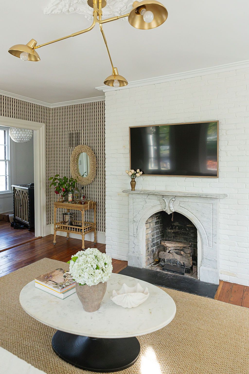 Modern living room with white brick fireplace, mounted TV, brass ceiling light, and oval marble coffee table on jute rug.
