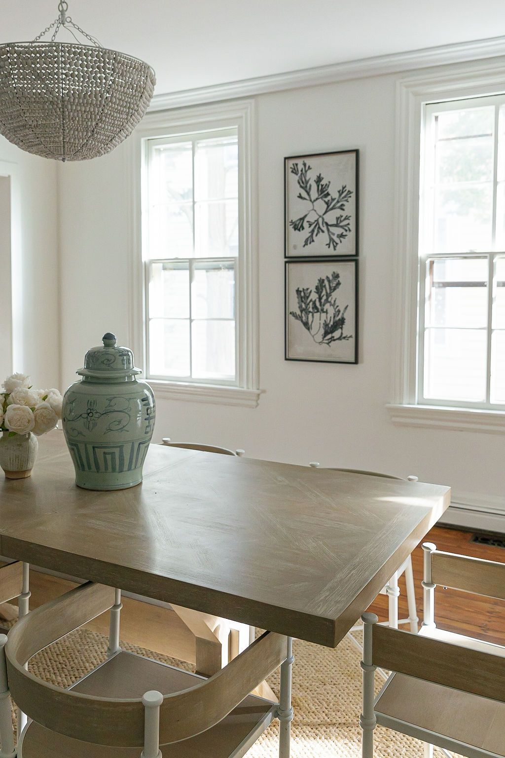 Elegant dining room with dark wood table, crystal chandelier, white walls, framed artwork and seafoam green ginger jars.