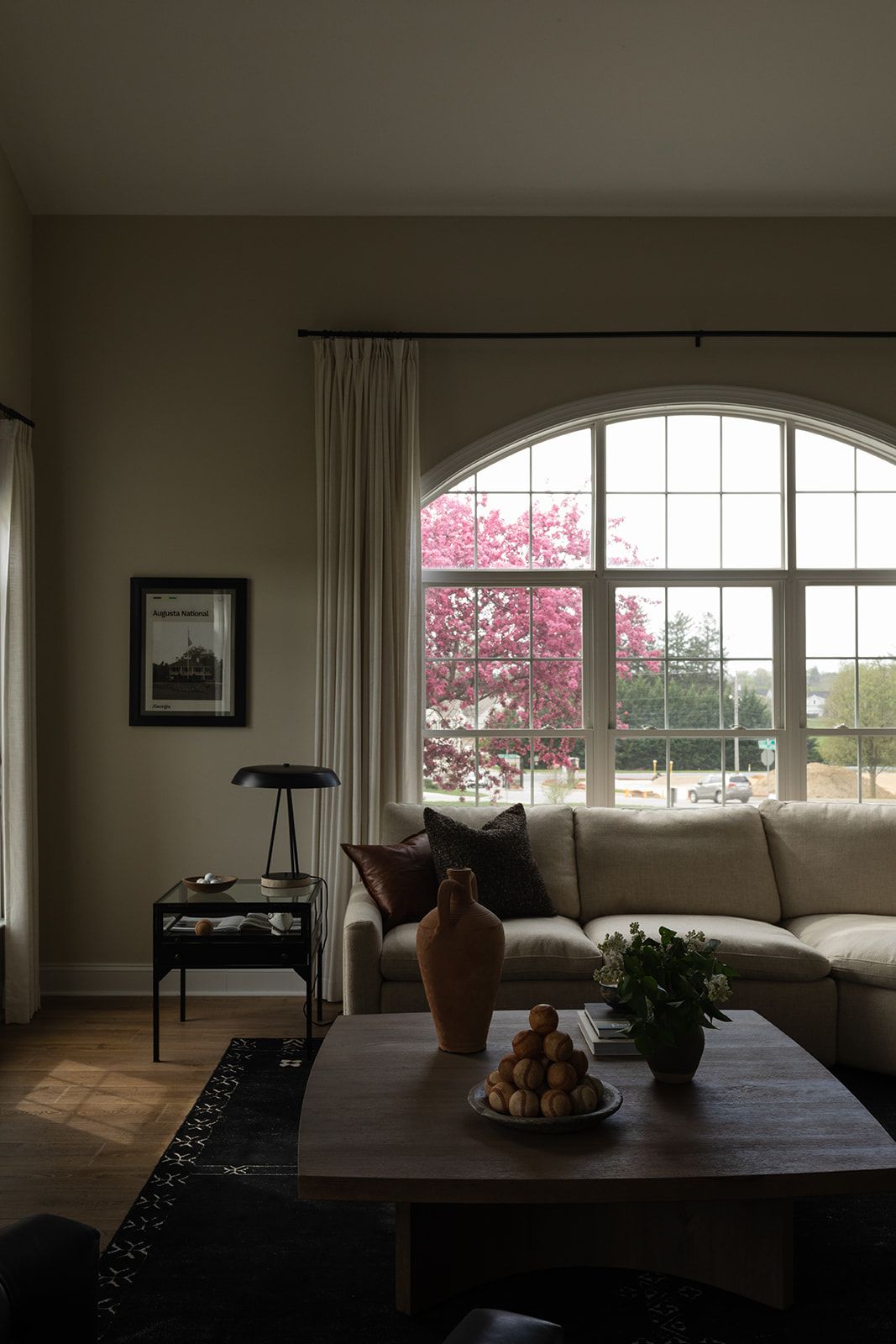 Living room with arched windows, white curtains, and pink cherry blossoms visible outside.